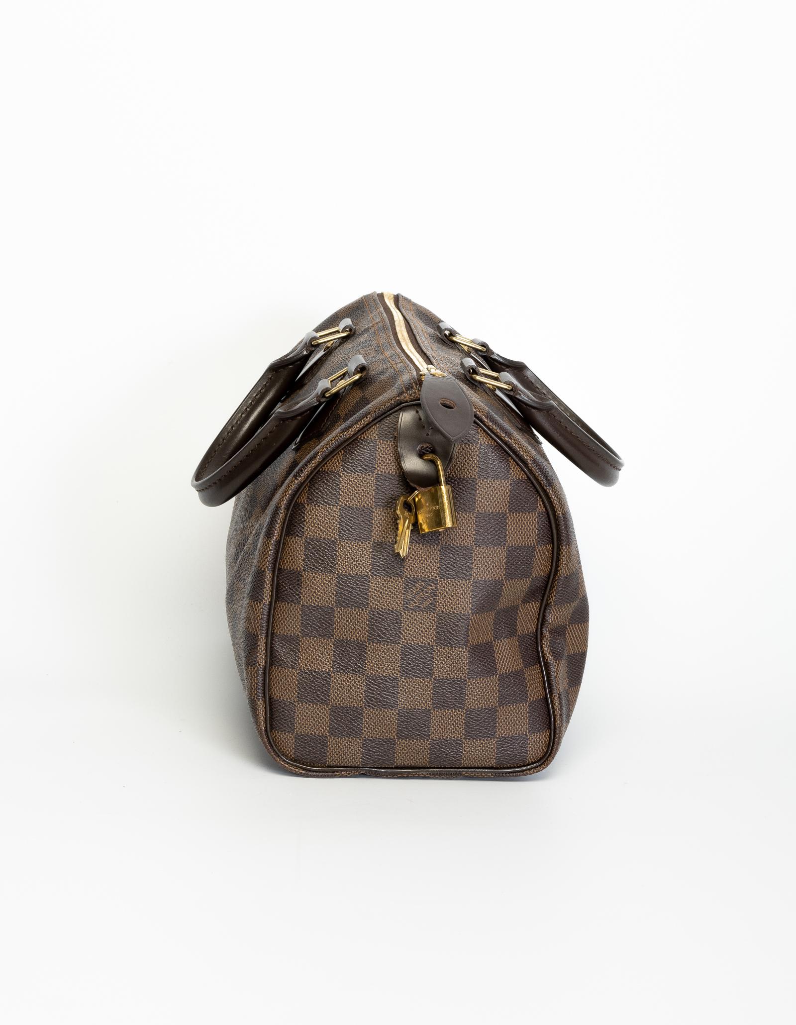 Speedy 25cm. This Speedy 25 is made of Damier Ebene canvas and features leather finishes, rolled leather handles, brass hardware, top zip closure & red fabric interior lining. (Damier is French for checkerboard)
**Authenticated by entrupy**

COLOR: