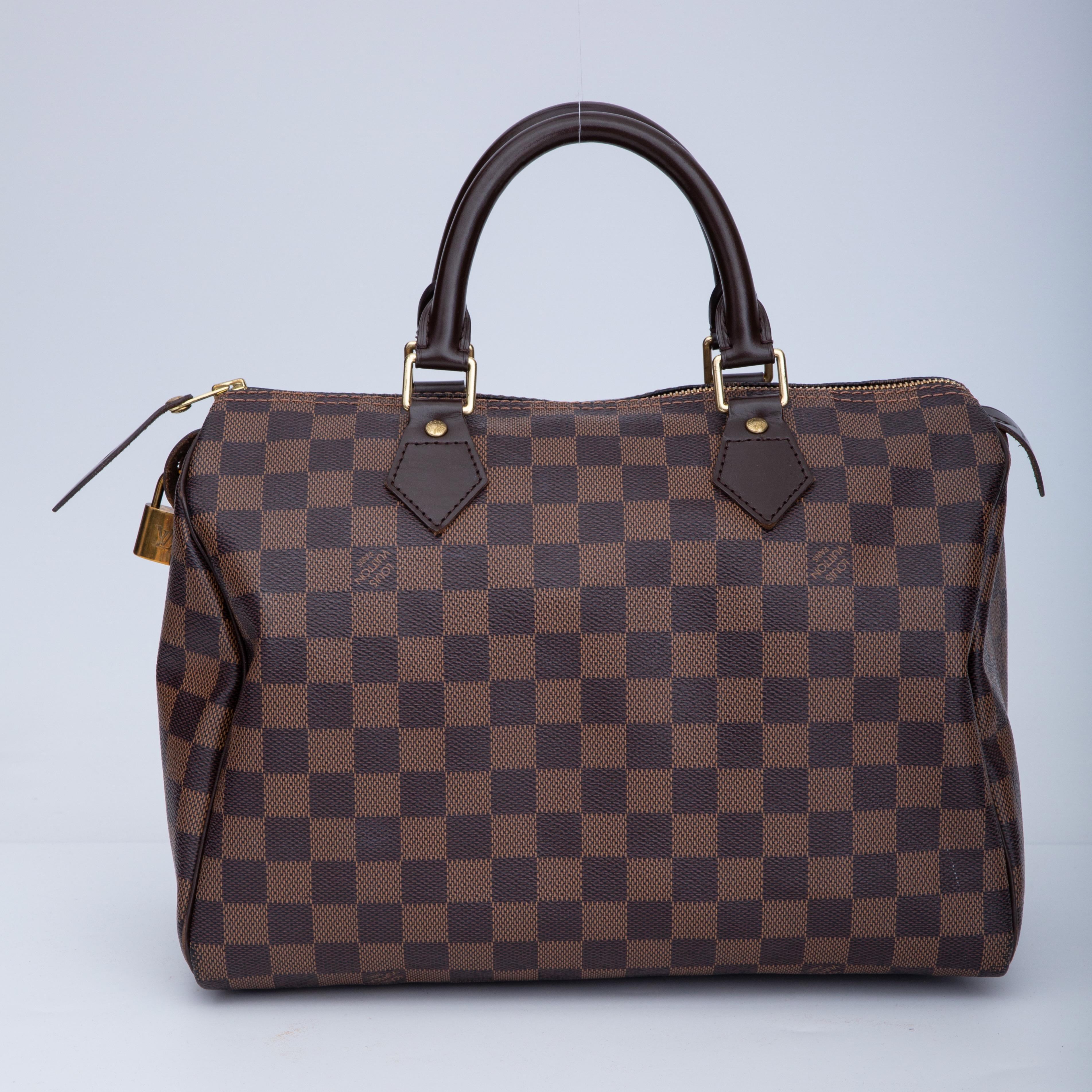 This handbag is constructed of signature Louis Vuitton damier checkered canvas in ebene brown. The bag features dark chocolate brown rolled leather top handles and trim with polished brass hardware. The top zipper opens to a bright red fabric