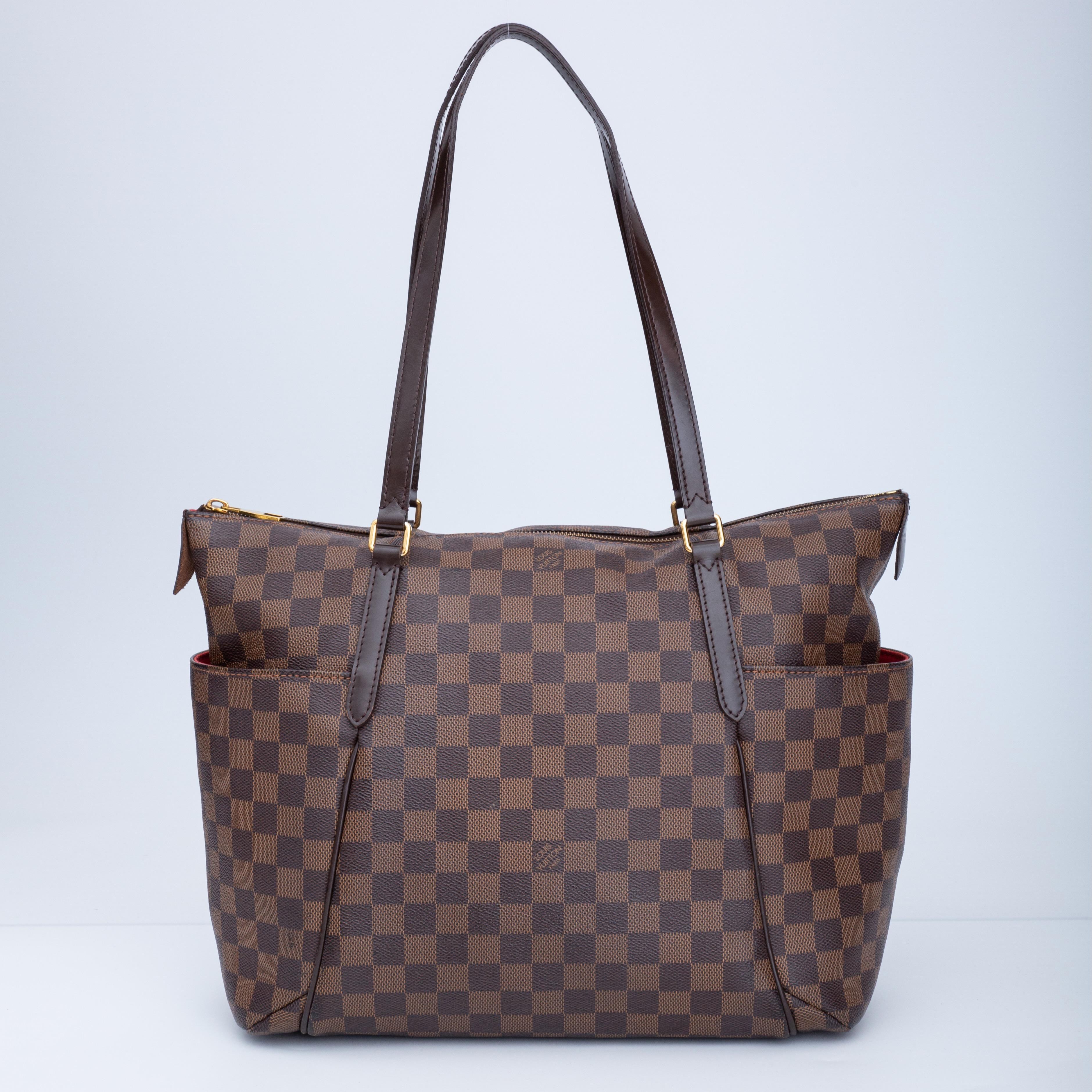 The bag is made with coated canvas with damier ebene print. Damier means checkerboard in French.This bag features dark brown leather shoulder straps, polished brass hardware, bucket pockets on the sides, top zip closure and a red fabric interior.