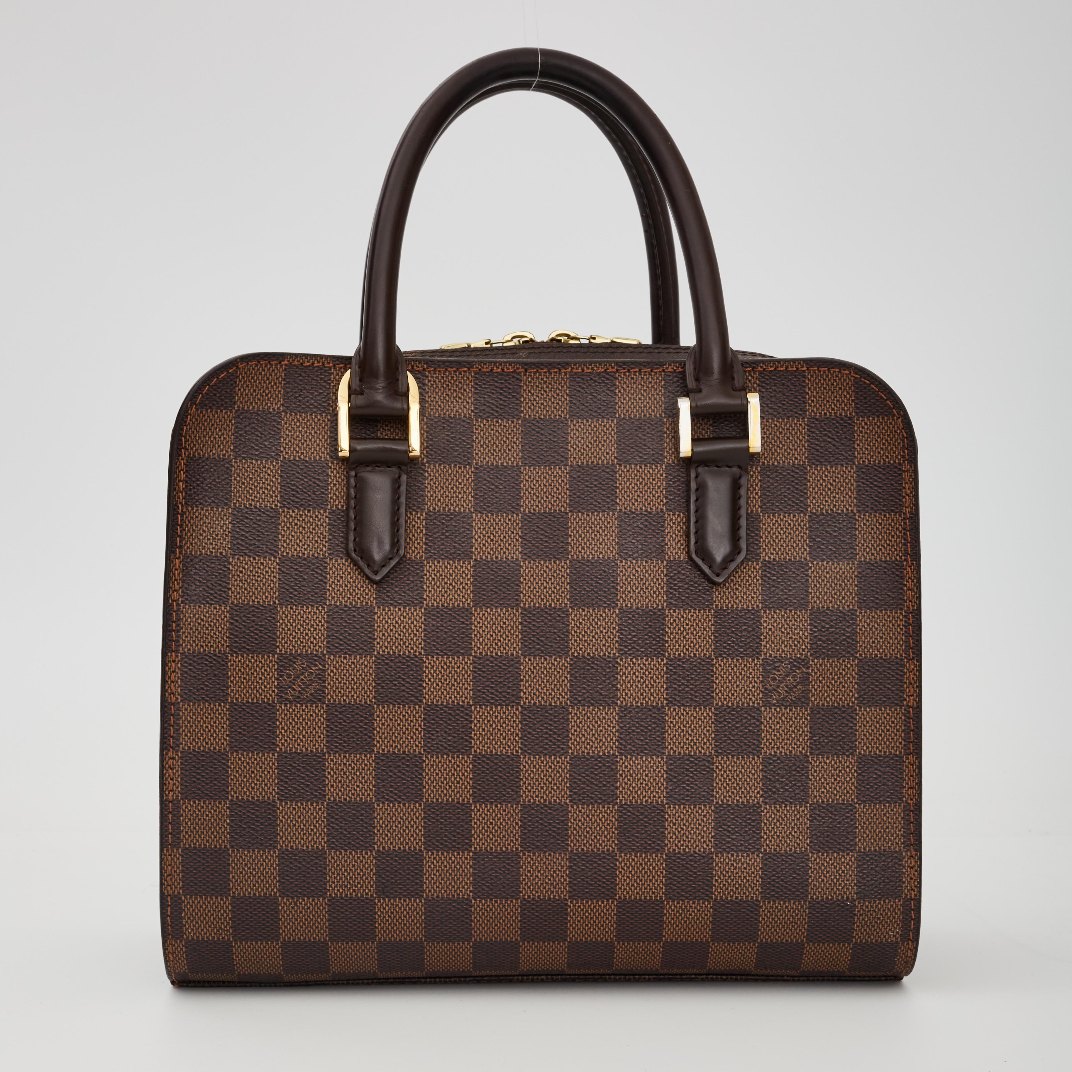 Questa borsa compatta è strutturata in tela damier toile, completata da finiture in pelle liscia marrone e da lati in pelle incrociata abbinati. La borsa presenta doppi manici in pelle arrotolati con maglie in ottone, finiture in pelle massiccia,