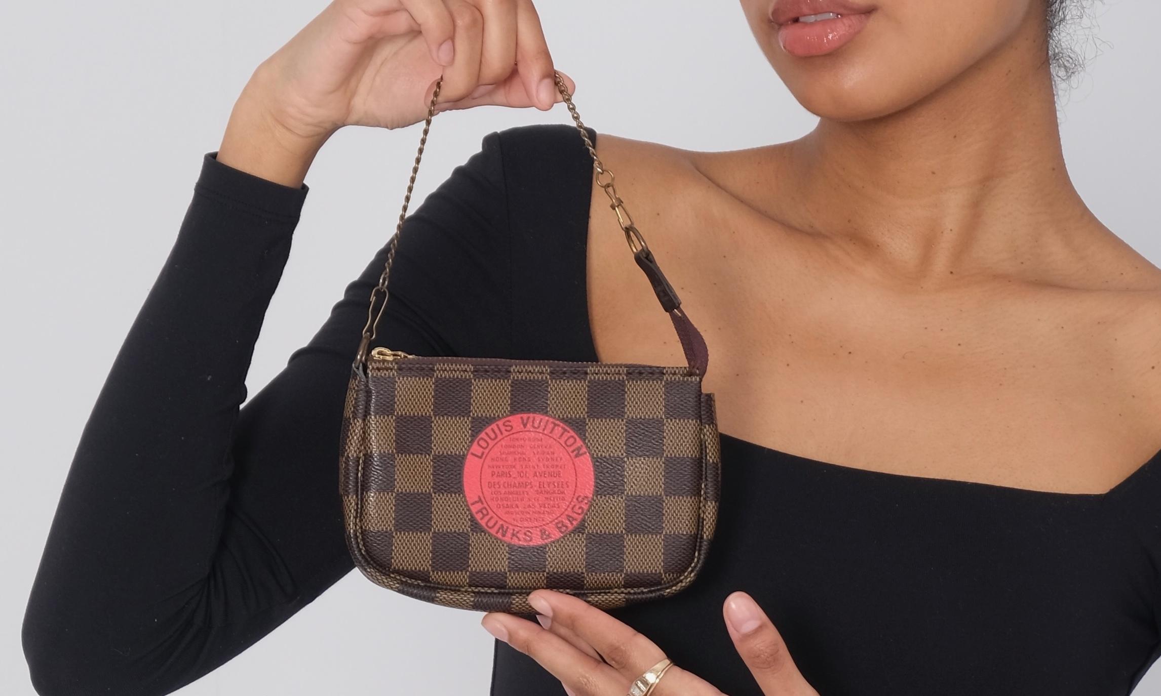 LV Complice Trunks & Bags Pochette Accessoires Mini. This pochette is made of Louis Vuitton signature damier canvas in brown, with a prominent red 