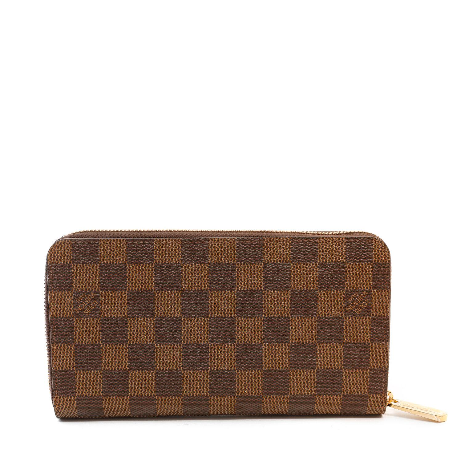 This authentic Louis Vuitton Damier Ebene Zippy Wallet is in pristine condition.   Signature LV checkered pattern in tobacco and deep brown with gold tone zipper.  Leather interior easily manages coins, cards and currency in an organized fashion. 