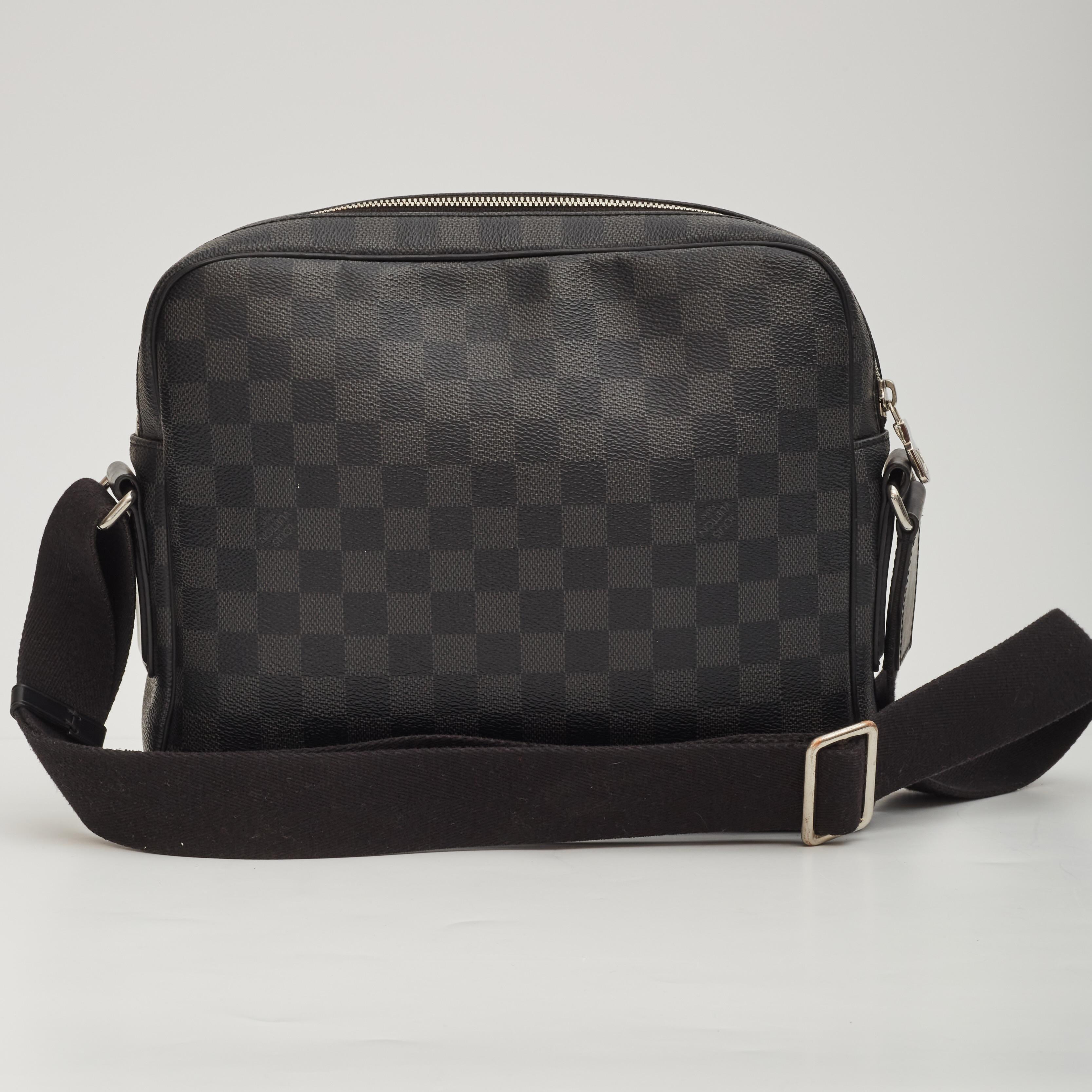 This messenger bag is made of Louis Vuitton signature Damier Graphite checkerd coated canvas. The bag features black leather trim, a woven fabric adjustable shoulder strap, silver tone hardware and a front zipper pocket. The top zippers open to a