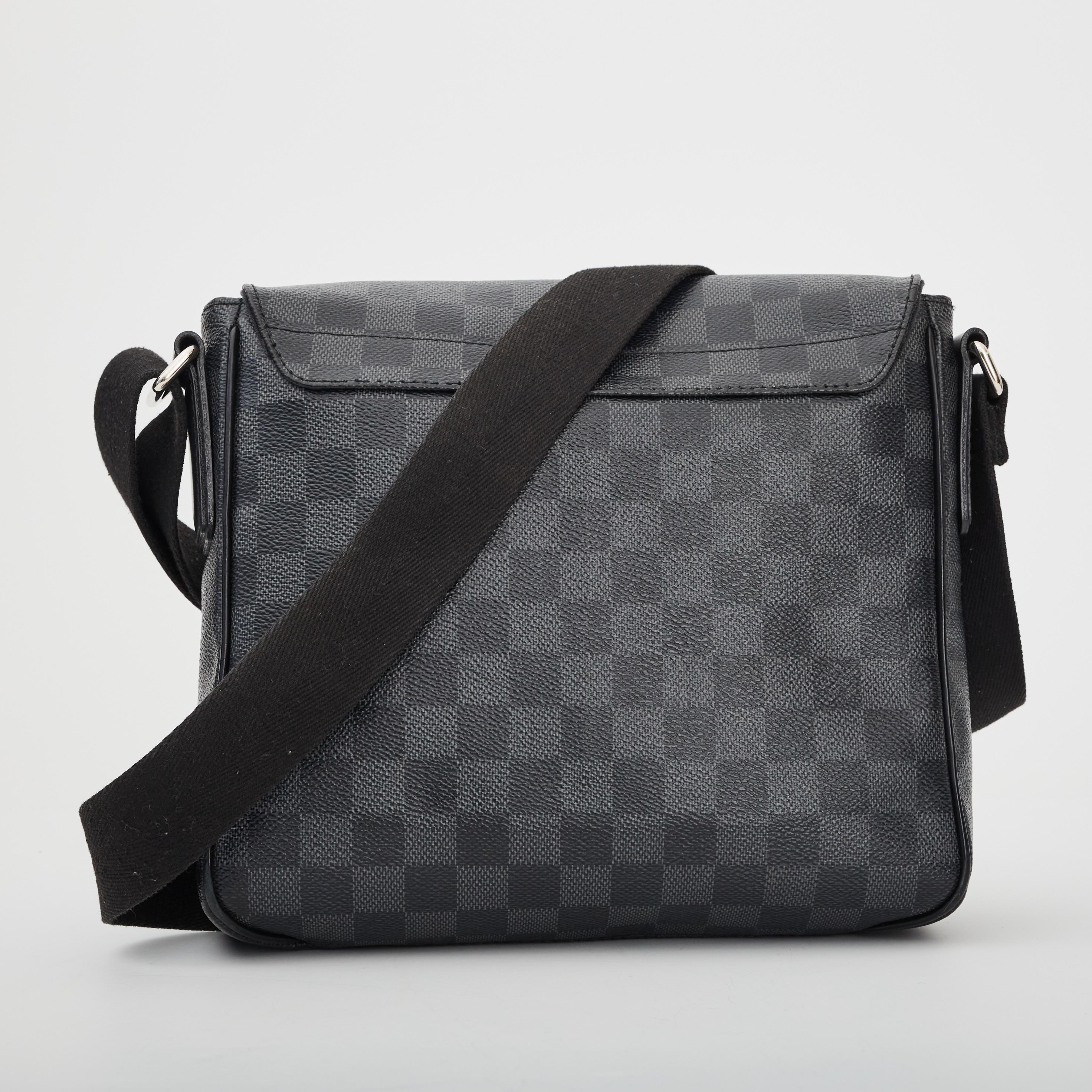 This messenger is made of graphite damier patterned canvas in graphite grey. The bag features a boxy rectangular shape with a large front flap with magnetic closure, black cowhide piping and an adjustable woven fabric cross-body strap. The flap