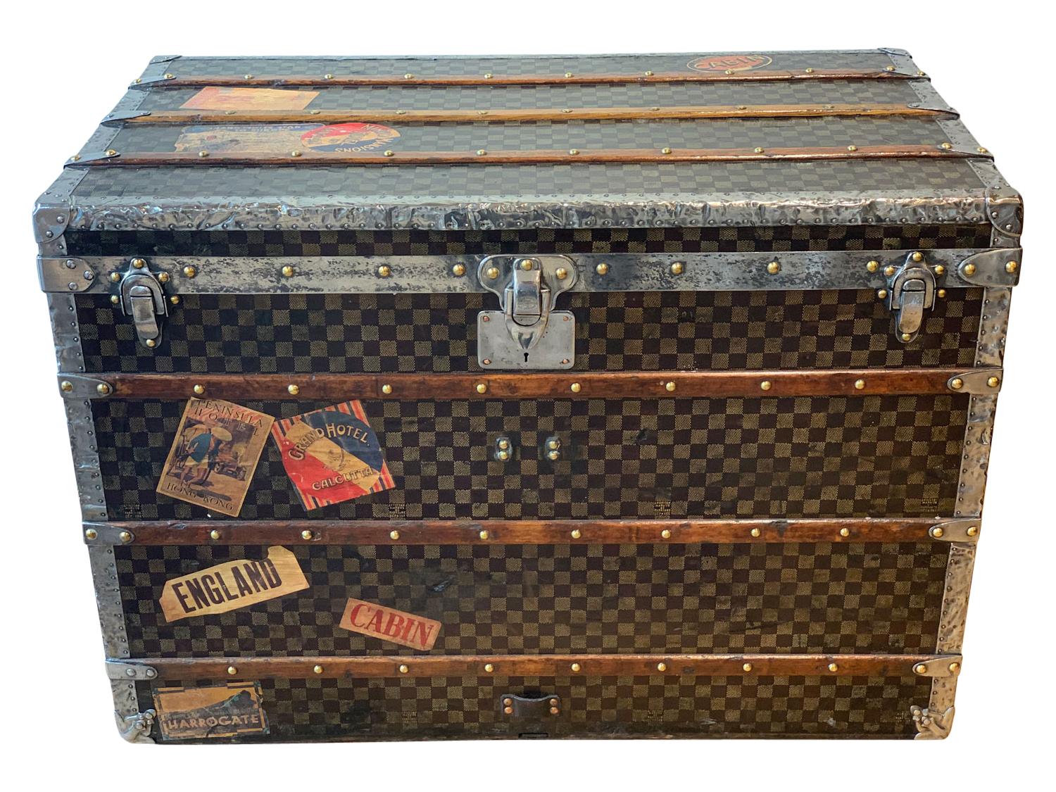 A Louis Vuitton Damier steamer trunk, circa 1905. The checkerboard pattern with steel bound hardware and steel handles, covered in original travel stickers. The design of Louis Vuitton’s Damier was the result of the creative spark that shined