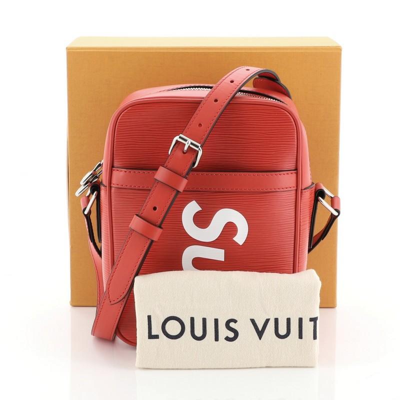 This Louis Vuitton Danube Handbag Limited Edition Supreme Epi Leather PM, crafted from red epi leather, features an adjustable strap, exterior front slip pocket, Supreme lettering, LV logo, and silver-tone hardware. Its top zip closure opens to a