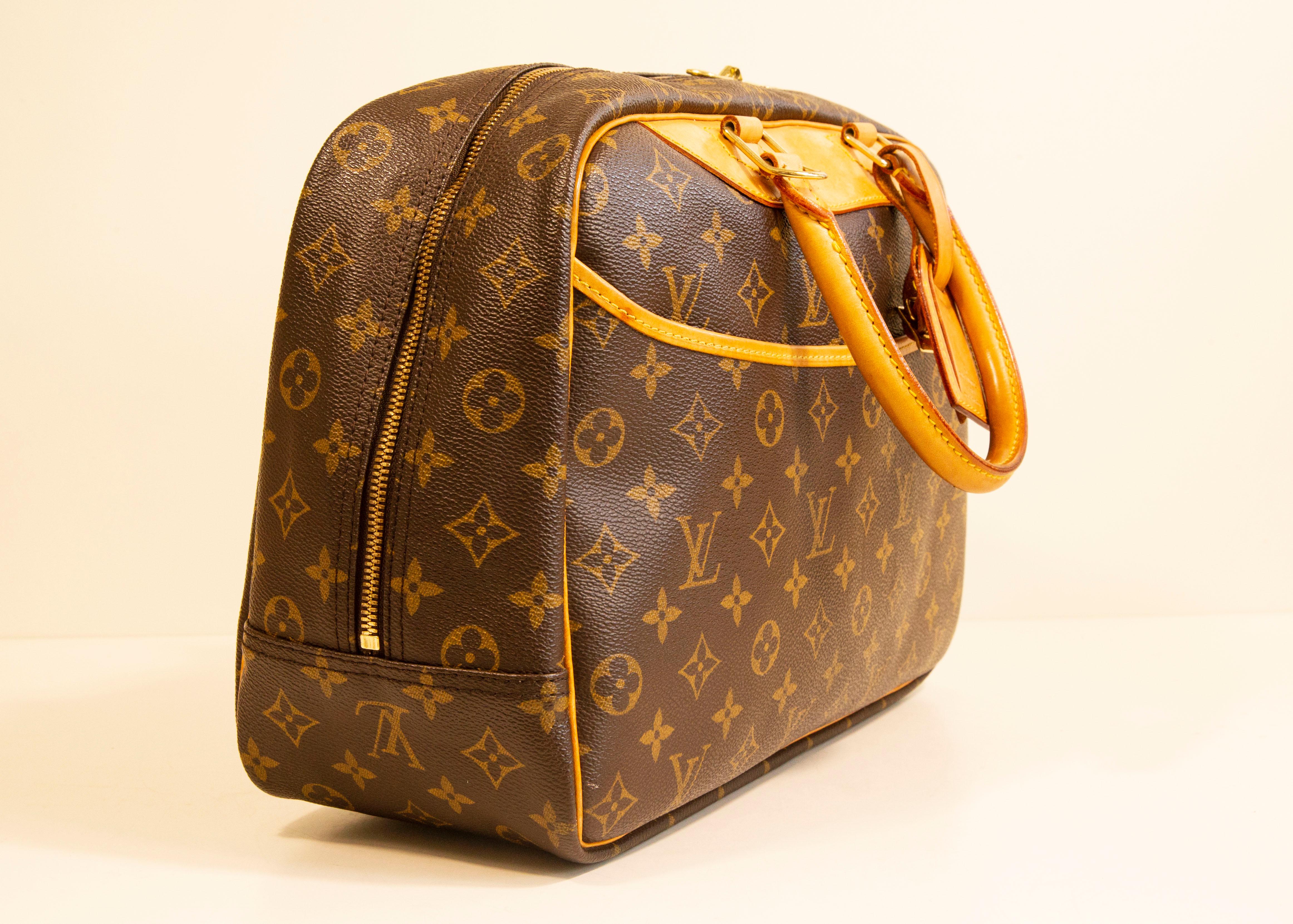 A vintage Deauville handbag by Louis Vuitton. The bag is made of brown monogram vinyl coated canvas with beige/light brown Vachetta leather trim and brass toned hardware. The interior is lined with beige synthetic fabric, and next to the major