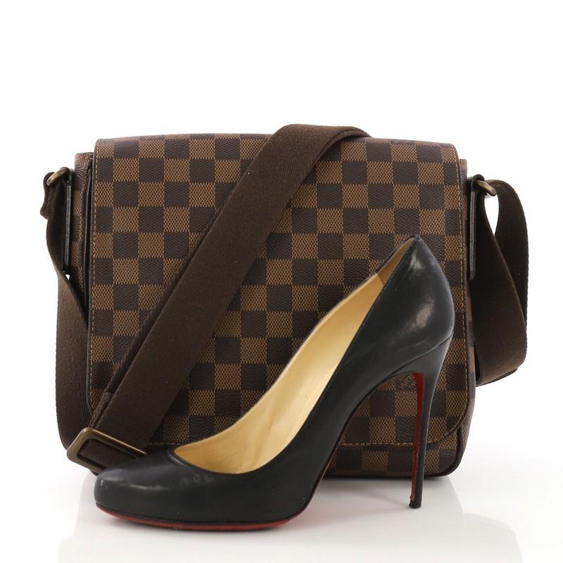 This Louis Vuitton District Messenger Bag Damier PM, crafted from damier ebene coated canvas, features an adjustable textile shoulder strap and matte bronze-tone hardware. Its flap opens to a brown fabric interior with slip pockets. Authenticity
