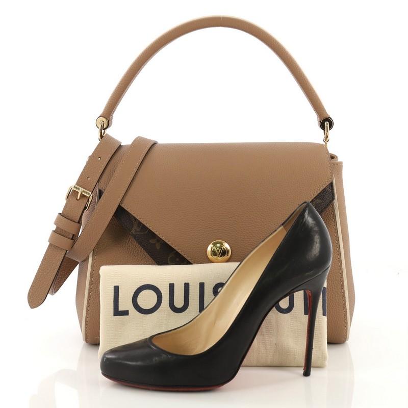 This Louis Vuitton Double V Handbag Calfskin and Monogram Canvas, crafted in beige calfskin and monogram coated canvas, features a rolled top handle, exterior back pocket, protective base studs, and gold-tone hardware. Its magnetic snap closure