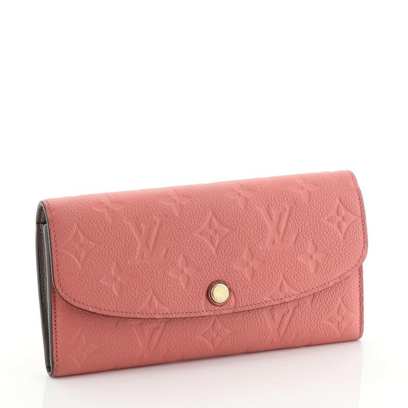 This Louis Vuitton Emilie Wallet Monogram Empreinte Leather, crafted from pink monogram empreinte leather, features a frontal flap and gold-tone hardware. Its snap button closure opens to a pink leather interior with multiple compartments and zip