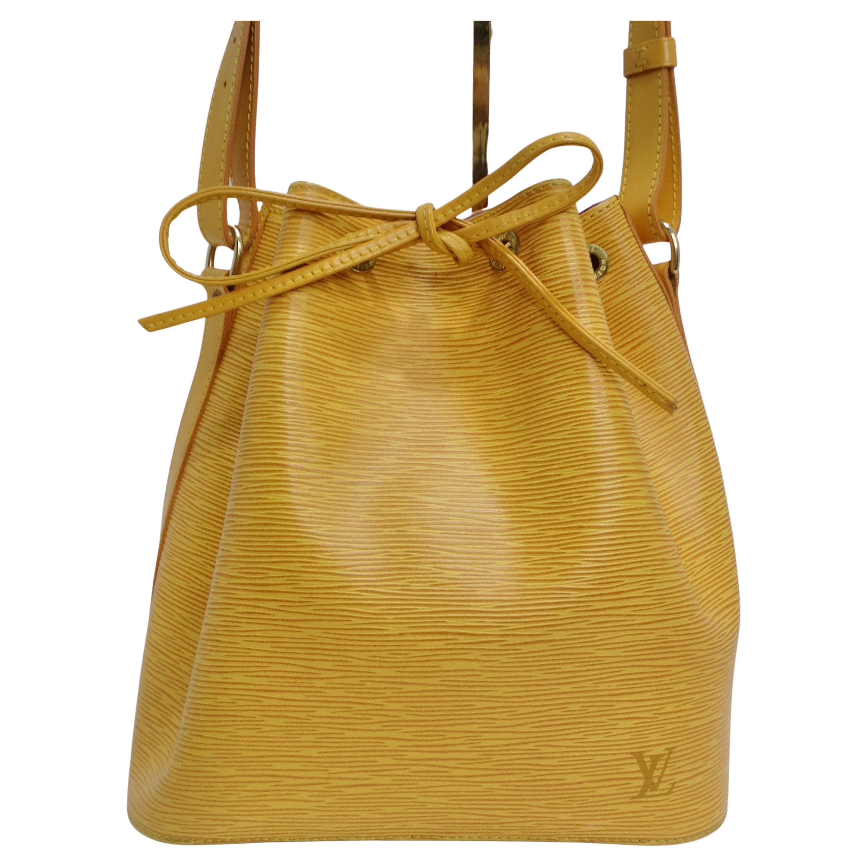 Introducing a timeless classic: the Louis Vuitton Epi Petite Noe Shoulder Bag. Crafted in the iconic textured Epi leather, this bag showcases a vibrant and sunny yellow hue that exudes elegance and style. The bucket-style drawstring design adds a
