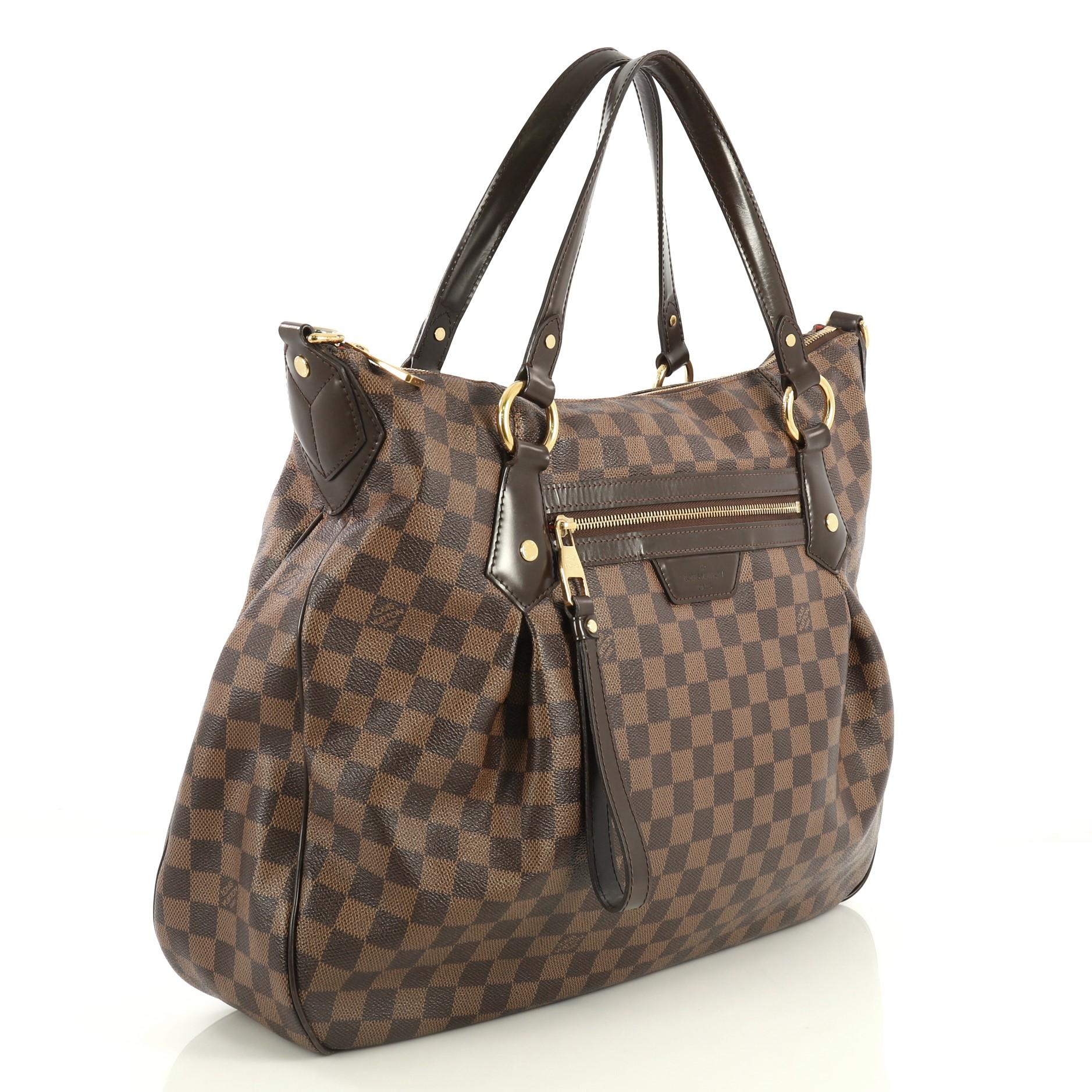 This Louis Vuitton Evora Handbag Damier GM, crafted in damier ebene coated canvas, features vachetta leather strap and trim, pleated silhouette, front zip pocket, and gold-tone hardware. Its zip closure opens to a red microfiber interior with slip