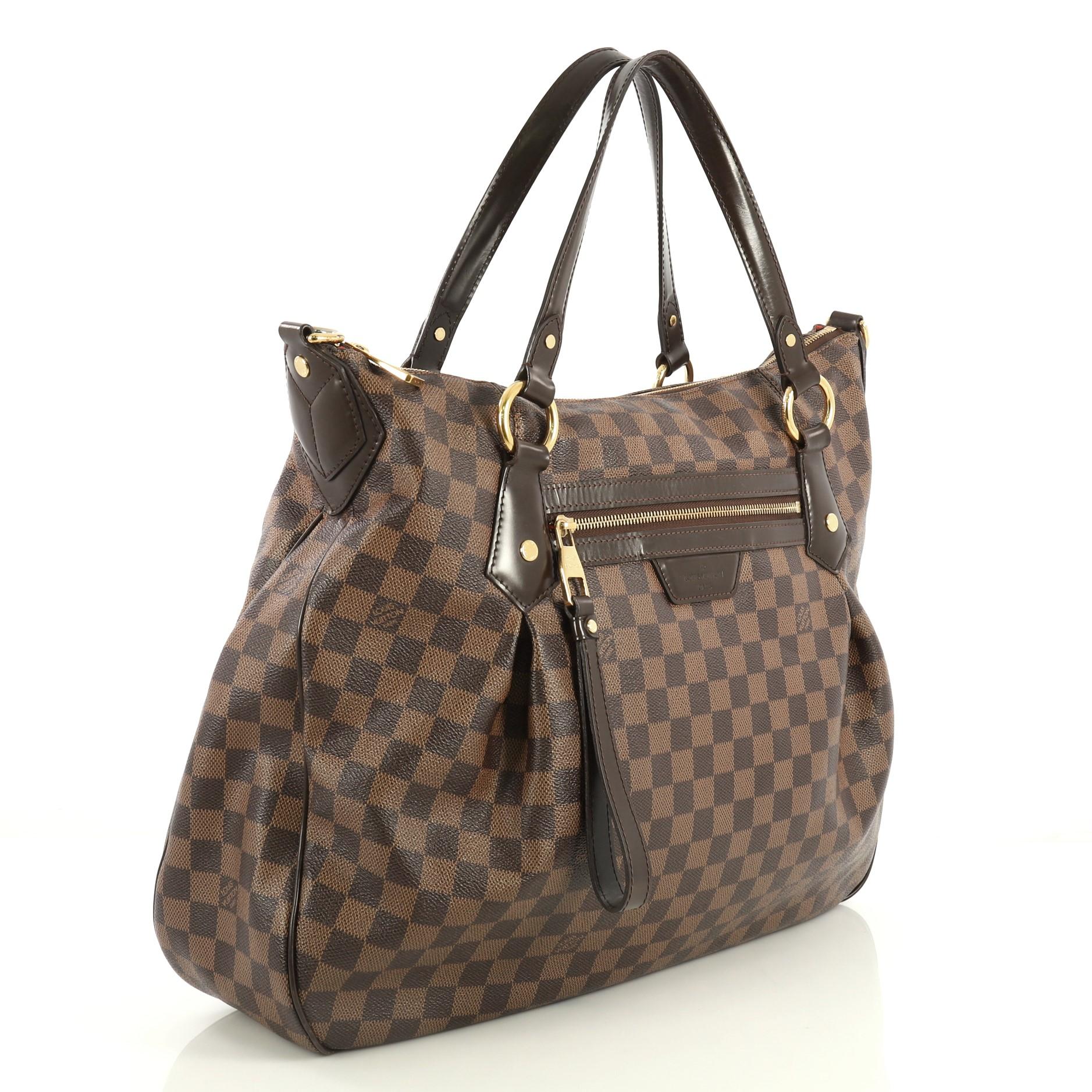 This Louis Vuitton Evora Handbag Damier GM, crafted in damier ebene coated canvas, features vachetta leather strap and trim, pleated silhouette, front zip pocket, and gold-tone hardware. Its zip closure opens to a red microfiber interior with slip