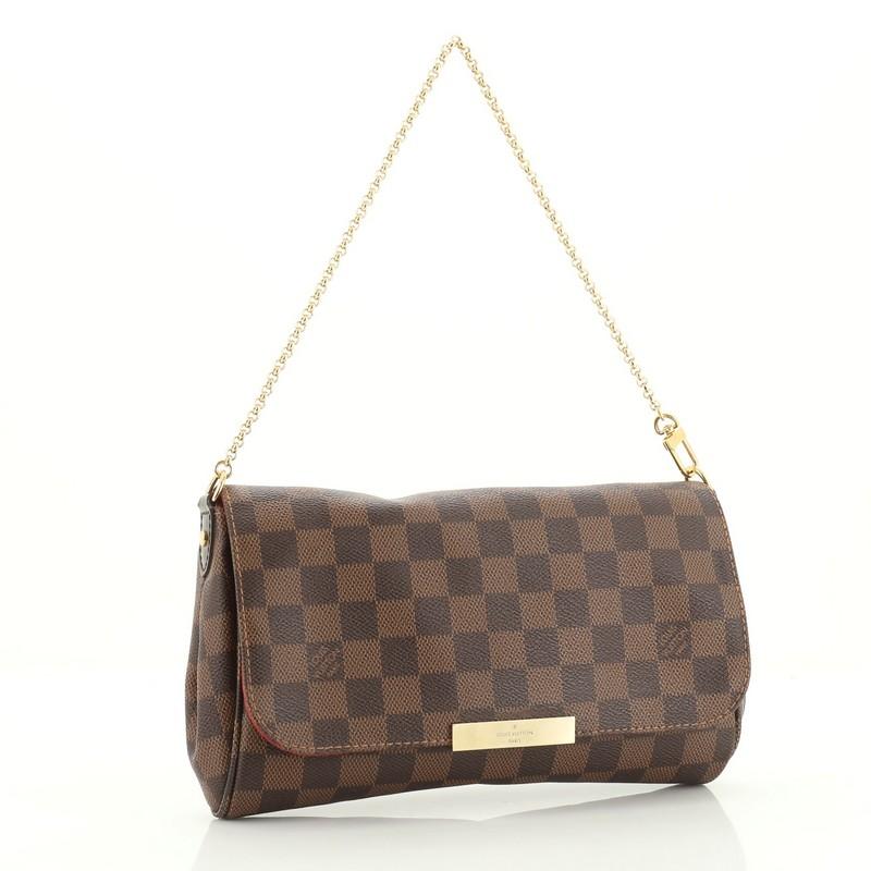 This Louis Vuitton Favorite Handbag Damier MM, crafted in damier ebene coated canvas, features a long leather strap, wristlet chain, LV plated logo and gold-tone hardware. Its flap closure opens to a red fabric interior with slip pocket.