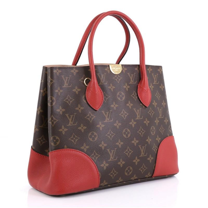 This Louis Vuitton Flandrin Handbag Monogram Canvas, crafted from brown monogram coated canvas, features dual rolled leather handles, red leather trim, and gold-tone hardware. It opens to a beige microfiber interior with a center zip compartment.