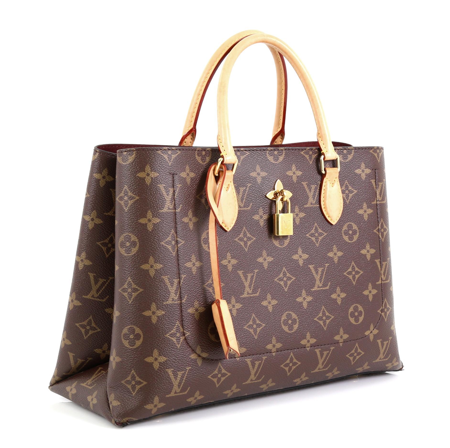 This Louis Vuitton Flower Tote Monogram Canvas, crafted from brown monogram coated canvas, features dual rolled handles, front pocket with monogram flower and padlock, protective base studs and gold-tone hardware. It opens to a purple microfiber