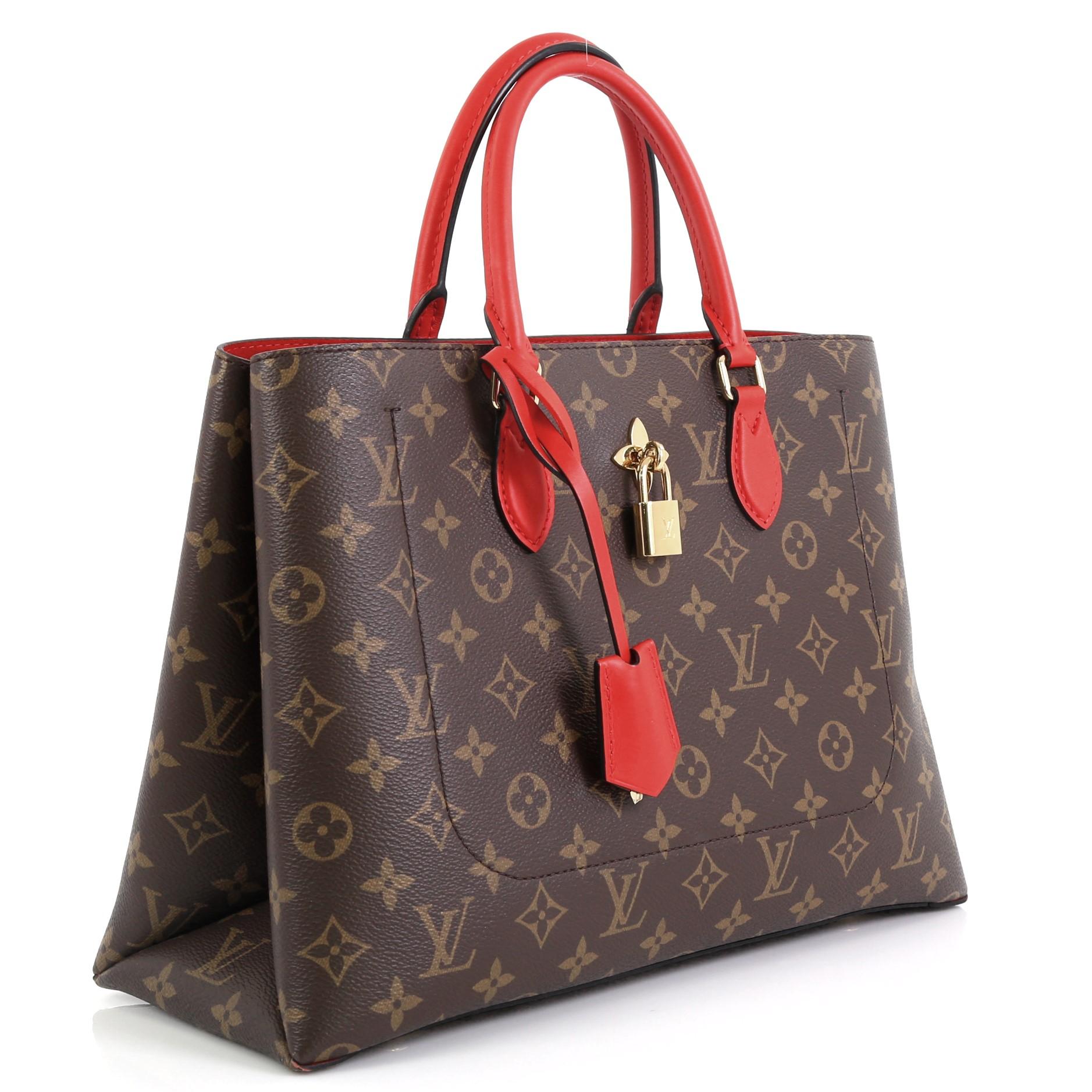 This Louis Vuitton Flower Tote Monogram Canvas, crafted in brown monogram coated canvas, features dual rolled leather handles, monogram flower padlock, and gold-tone hardware. It opens to a red microfiber interior with a center zip compartment and