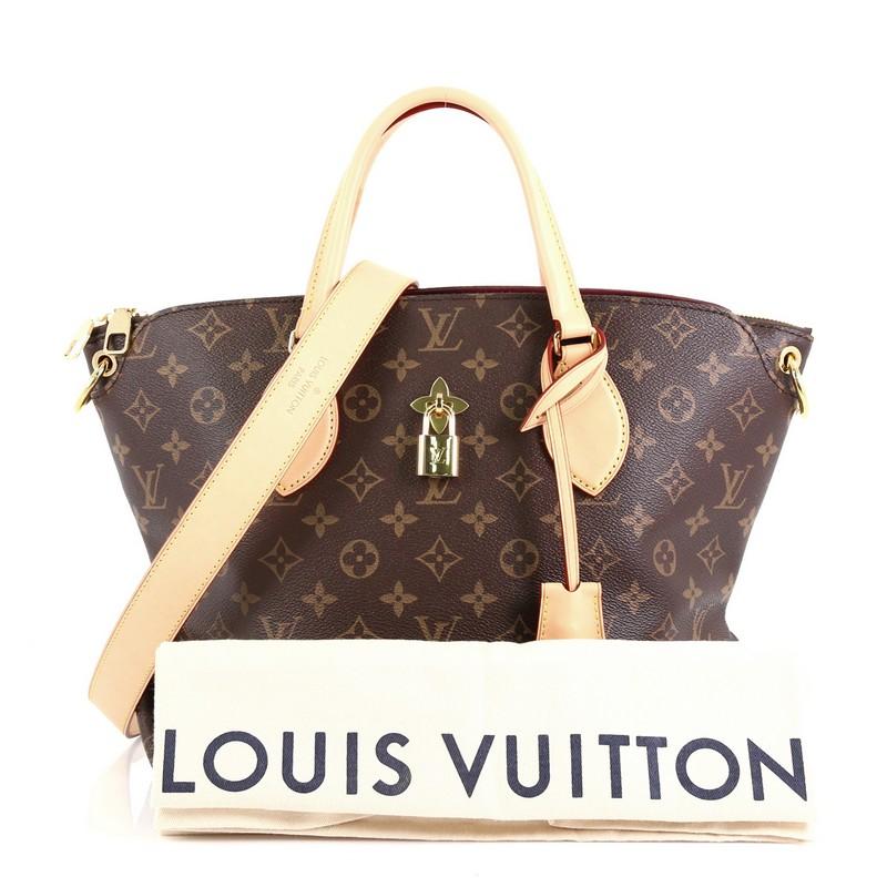 This Louis Vuitton Flower Zipped Tote Monogram Canvas MM, crafted in brown monogram coated canvas, features dual leather handles, turn lock with fleur detail, and gold-tone hardware. It opens to a partitioned purple microfiber interior with flat