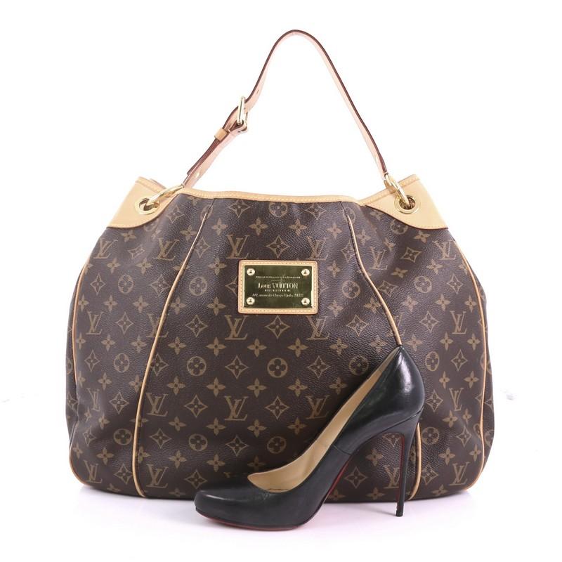 This Louis Vuitton Galliera Handbag Monogram Canvas GM, crafted from brown monogram coated canvas, features a looping leather strap, cowhide leather trims, and gold-tone hardware. Its magnetic snap closure opens to a beige microfiber interior with