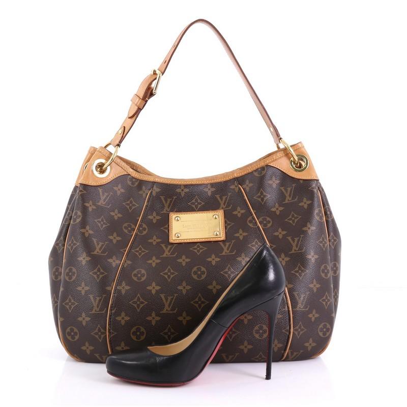 This Louis Vuitton Galliera Handbag Monogram Canvas PM, crafted in brown monogram coated canvas, features an adjustable shoulder strap, cowhide leather trim, and gold-tone hardware. Its magnetic snap closure opens to a beige microfiber interior with