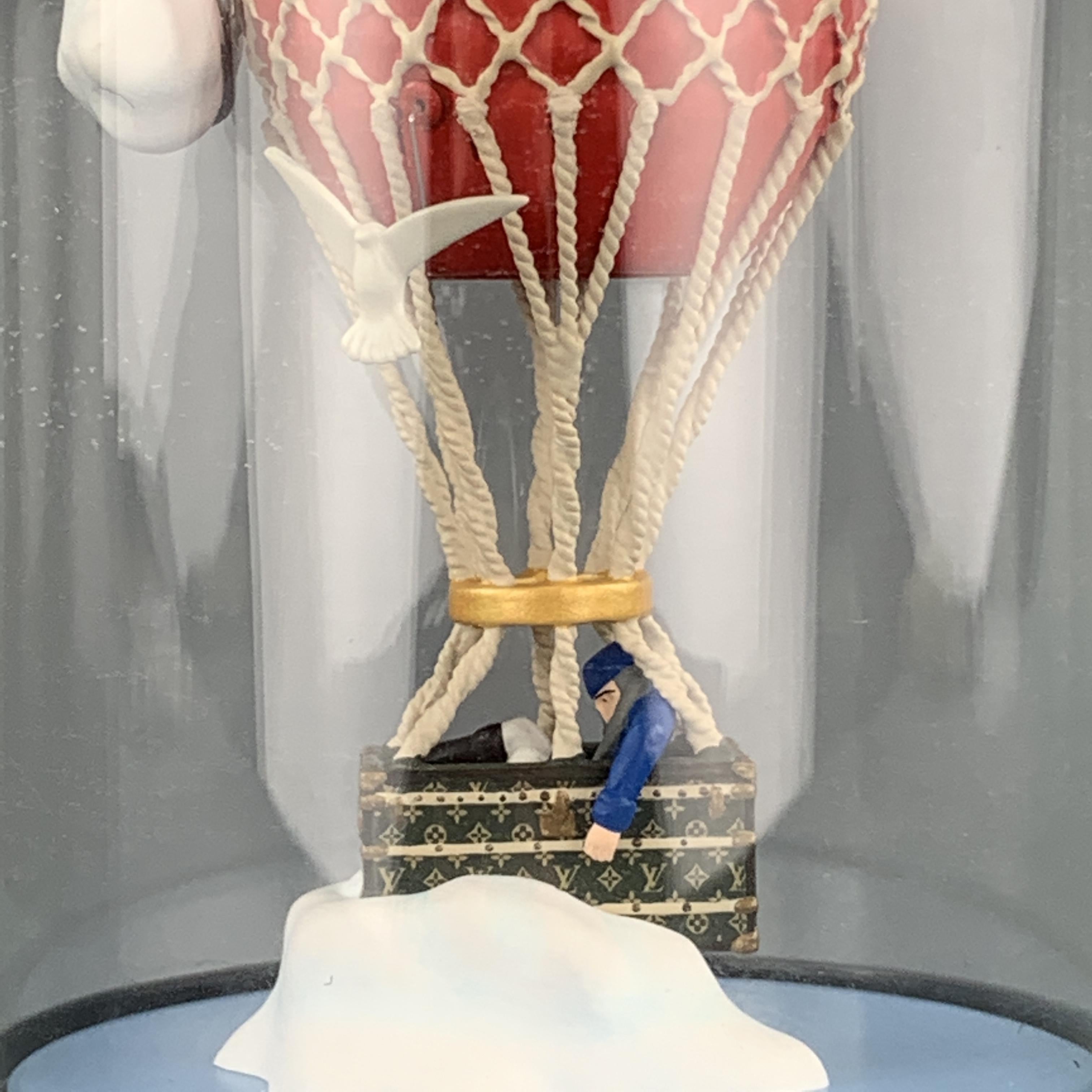 LOUIS VUITTON snow globe features a figurine of a man in a monogram trunk hot air balloon with cloud and birds in a glass dome with black logo base. Minor aging through glass. With original box.

Very Good Pre-Owned Condition.

Width: 8 cm.
Height: