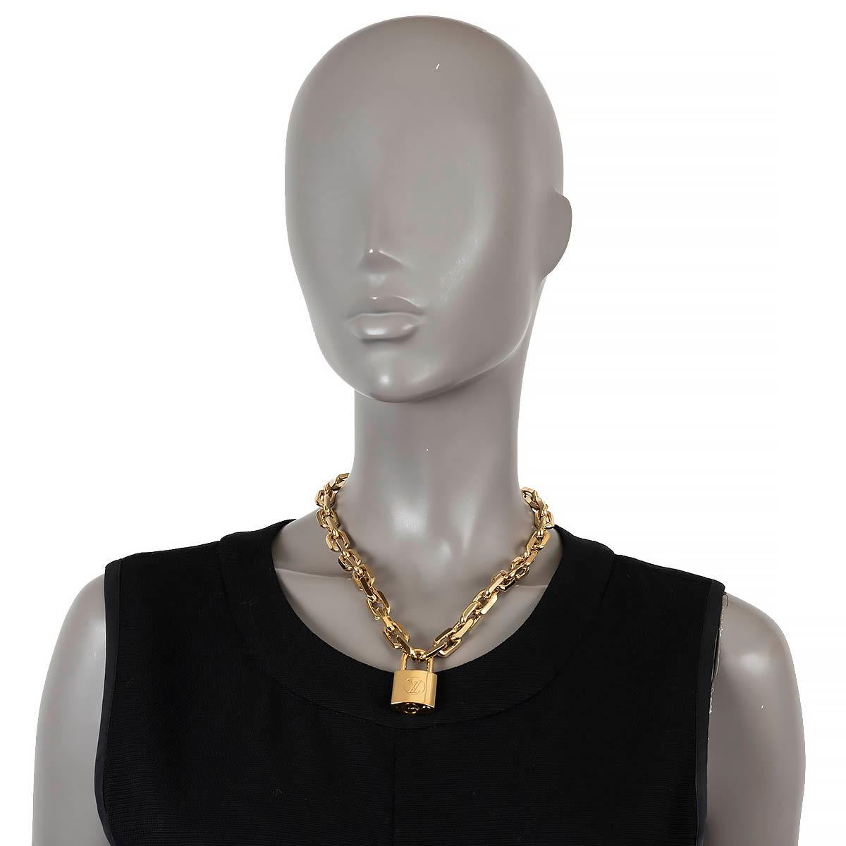 100% authentic Louis Vuitton Edge Cadenas necklace in gold-tone metal features a large padlock pendant meticulously engraved with the LV initials, suspended from a thick link chain. The pendant is opened and closed by pushing the lock. Has been worn