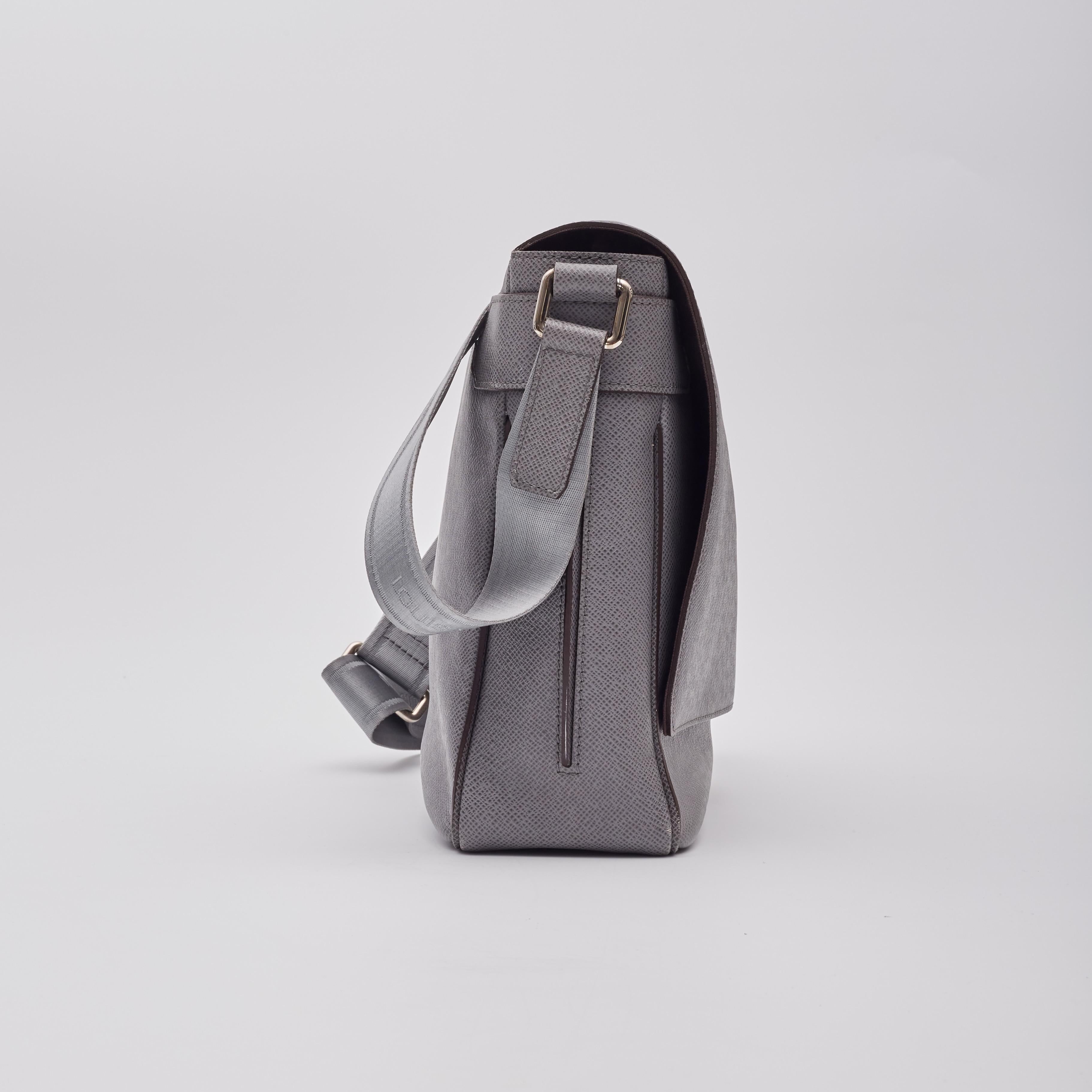Diese Umhängetasche ist aus grauem, quer genarbtem Leder gefertigt. Der verstellbare Schulterriemen aus Textil ist mit dem Louis-Logo versehen, und die Tasche hat einen Überschlag auf der Vorderseite, der zu einem Innenraum aus braunem Stoff mit