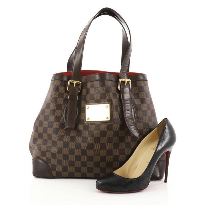 This authentic Louis Vuitton Hampstead Handbag Damier MM is the ultimate luxurious tote that showcases modern structure. Crafted from brands damier ebene coated canvas, this tote features dual tall flat leather handles with buckle details, brown