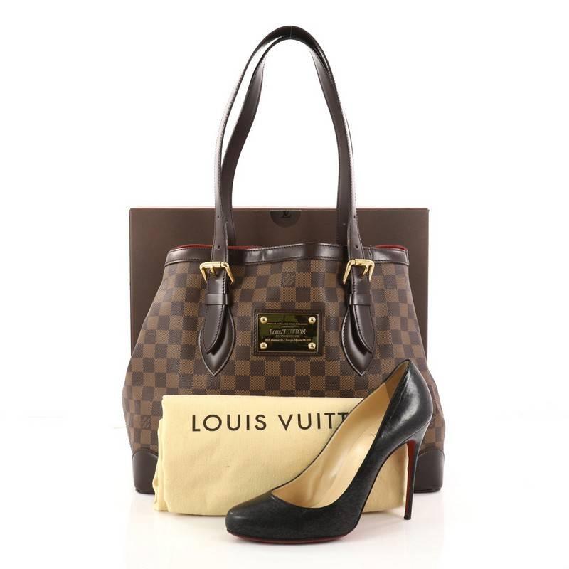 This authentic Louis Vuitton Hampstead Handbag Damier MM is the ultimate luxurious tote that showcases a modern structure. Crafted from damier ebene coated canvas, this tote features dual tall flat leather handles with buckle details, brown leather