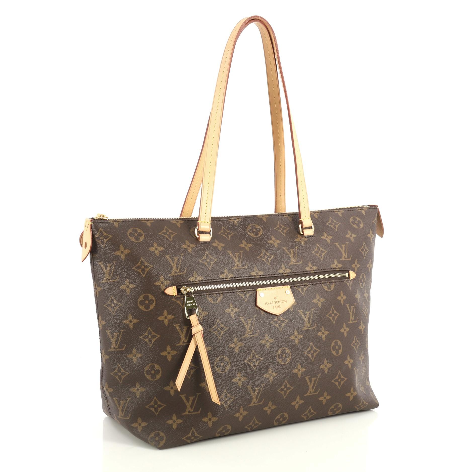 This Louis Vuitton Iena Tote Monogram Canvas MM, crafted from brown monogram coated canvas, features dual flat leather handles, exterior zip pocket, and gold-tone hardware. Its zip closure opens to a purple fabric interior with slip pockets.