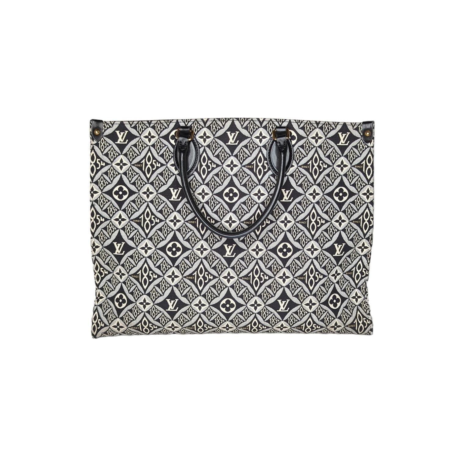 This chic tote is crafted of black, white and Gray Jacquard Since 1854 textile. The shoulder bag features black rolled leather top handles, black cowhide leather shoulder straps, and brass hardware. The top opens to a black microfiber interior with