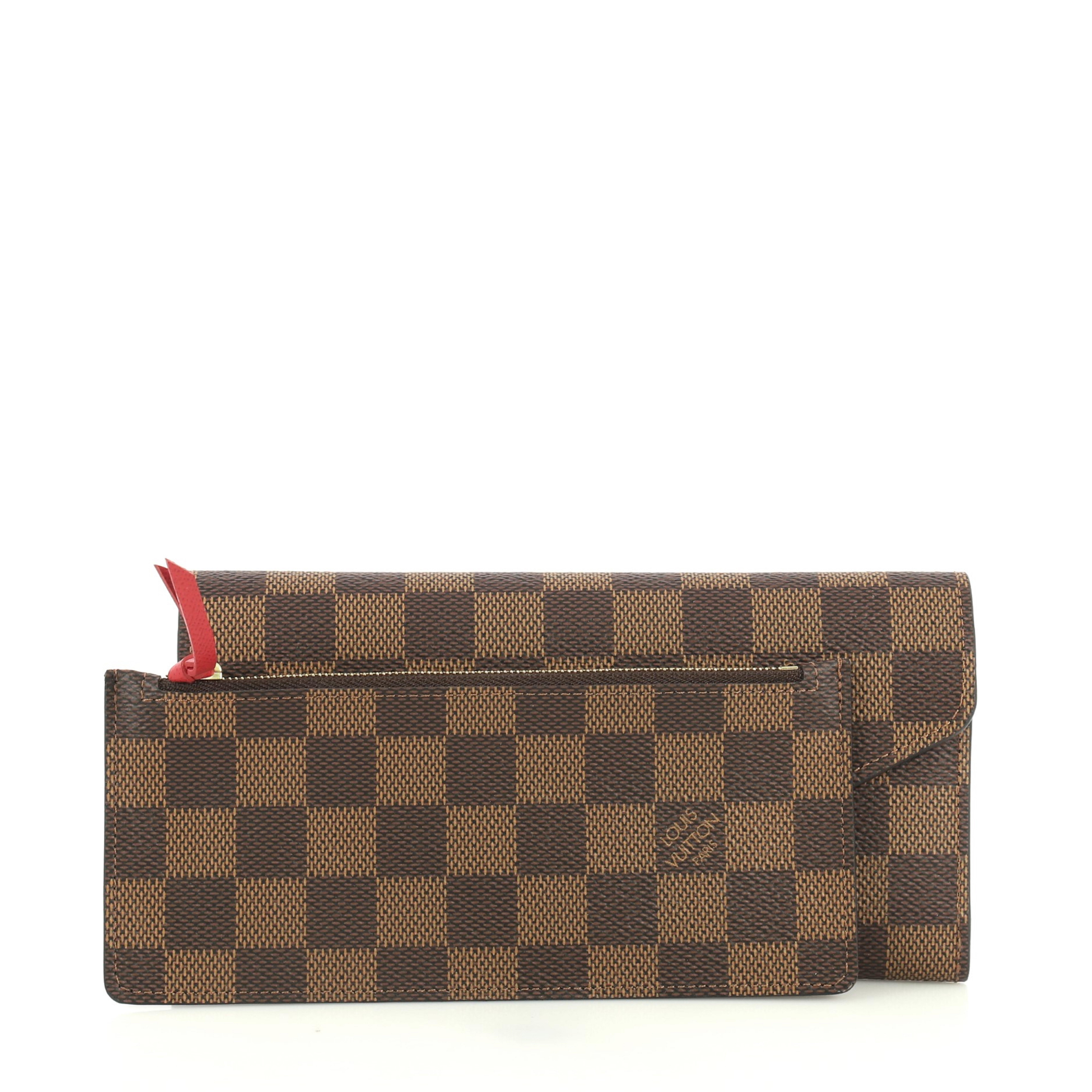 This Louis Vuitton Josephine Wallet NM Damier, crafted in damier ebene coated canvas, features gold-tone hardware. Its snap button closure opens to a red leather and damier ebene coated canvas interior with two large compartments and multiple card