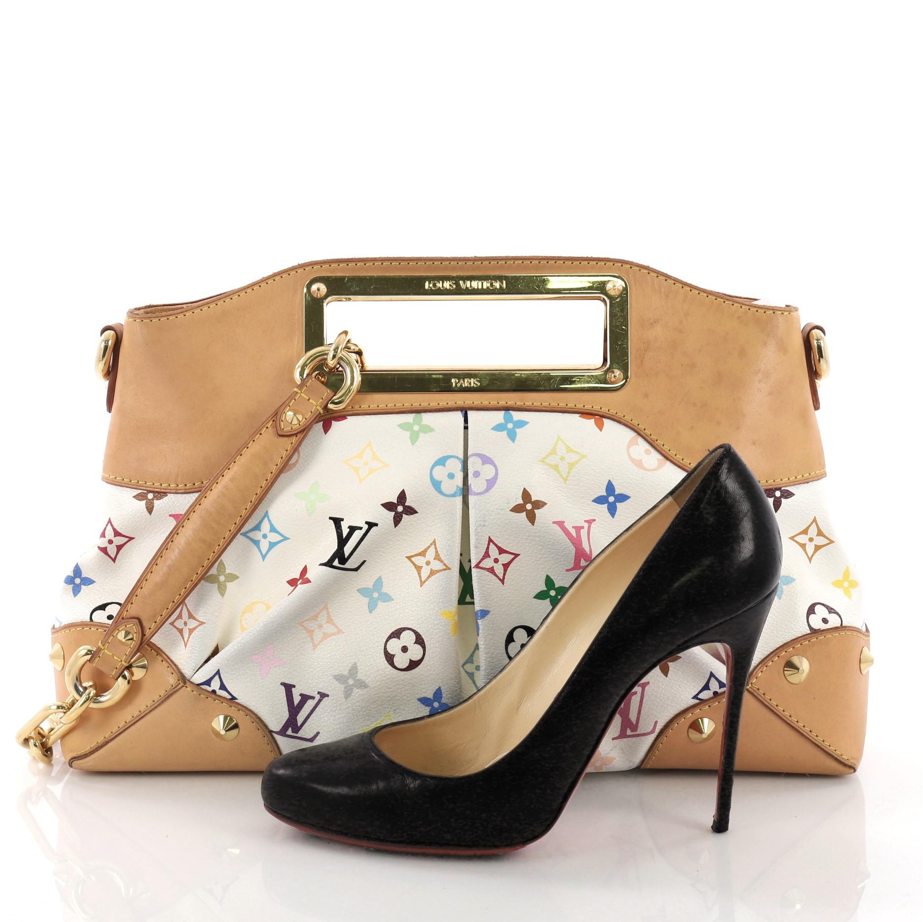 This Louis Vuitton Judy Handbag Monogram Multicolor MM, crafted from white monogram multicolor coated canvas, features a logo engraved cut-out handle, multiple gold studs, and gold-tone hardware. Its magnetic snap closure opens to a red microfiber