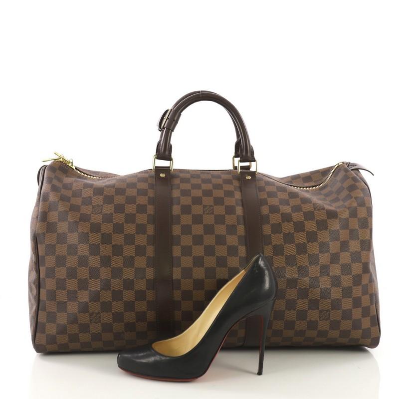 This Louis Vuitton Keepall Bag Damier 50, crafted in damier ebene coated canvas, features dual rolled handles and gold-tone hardware. Its dual zip closure opens to a brown fabric interior. Authenticity code reads: MB2077. **Note: Shoe photographed