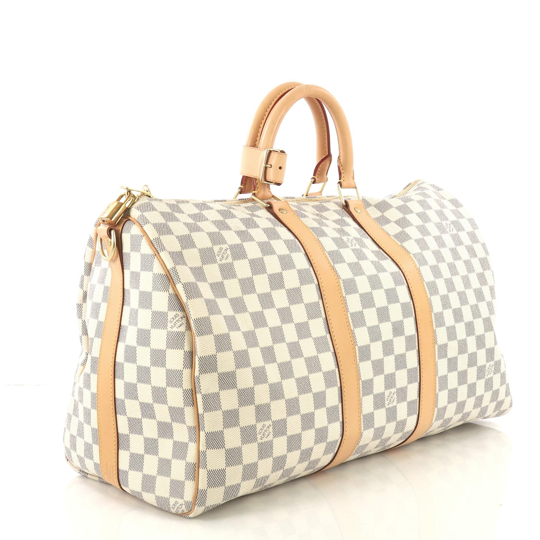 This Louis Vuitton Keepall Bandouliere Bag Damier 45, crafted from damier azur coated canvas, features dual rolled handles, vachetta leather trim, and gold-tone hardware. Its two-way top zip closure opens to a beige fabric interior. Authenticity