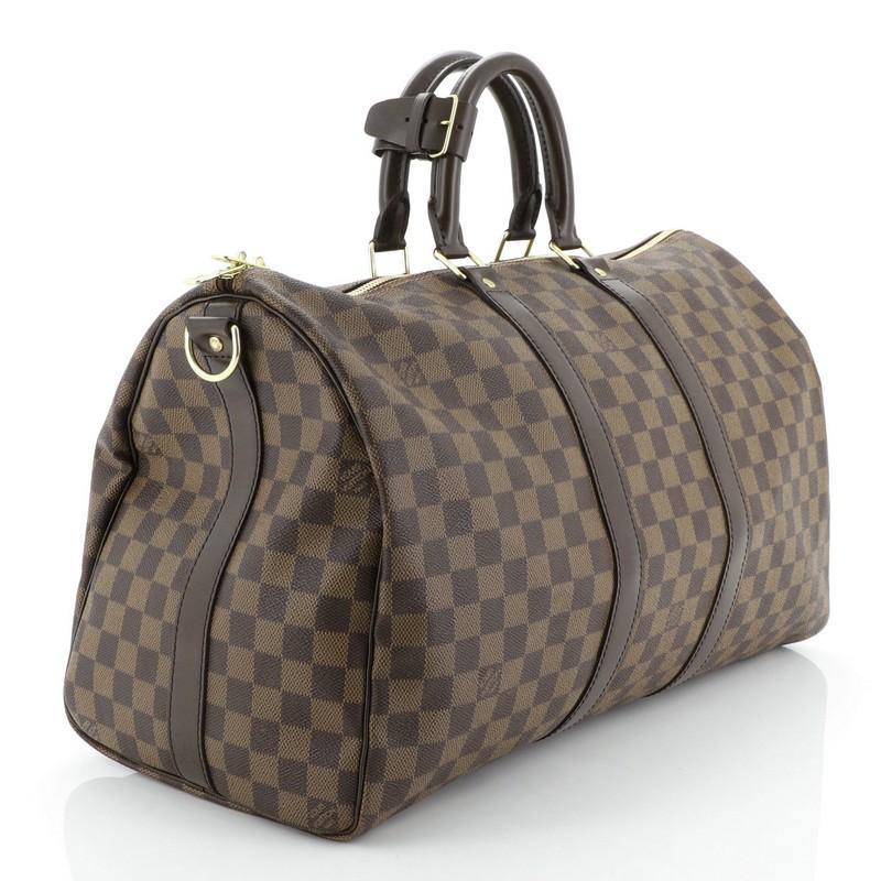This Louis Vuitton Keepall Bandouliere Bag Damier 45, crafted from damier ebene coated canvas, features dual rolled handles, leather trim, and gold-tone hardware. Its two-way top zip closure opens to a brown fabric interior. Authenticity code reads: