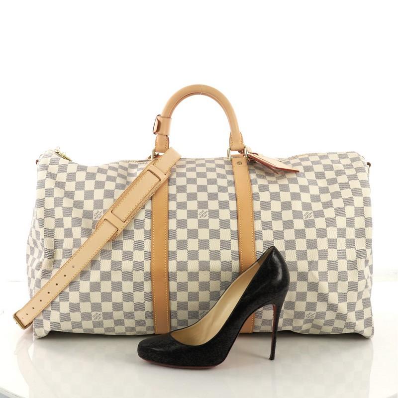 This Louis Vuitton Keepall Bandouliere Bag Damier Graphite 55, crafted with damier graphite coated canvas, features dual rolled handles, black leather trims, and gold-tone hardware. Its top zip closure opens to a beige fabric interior . Authenticity
