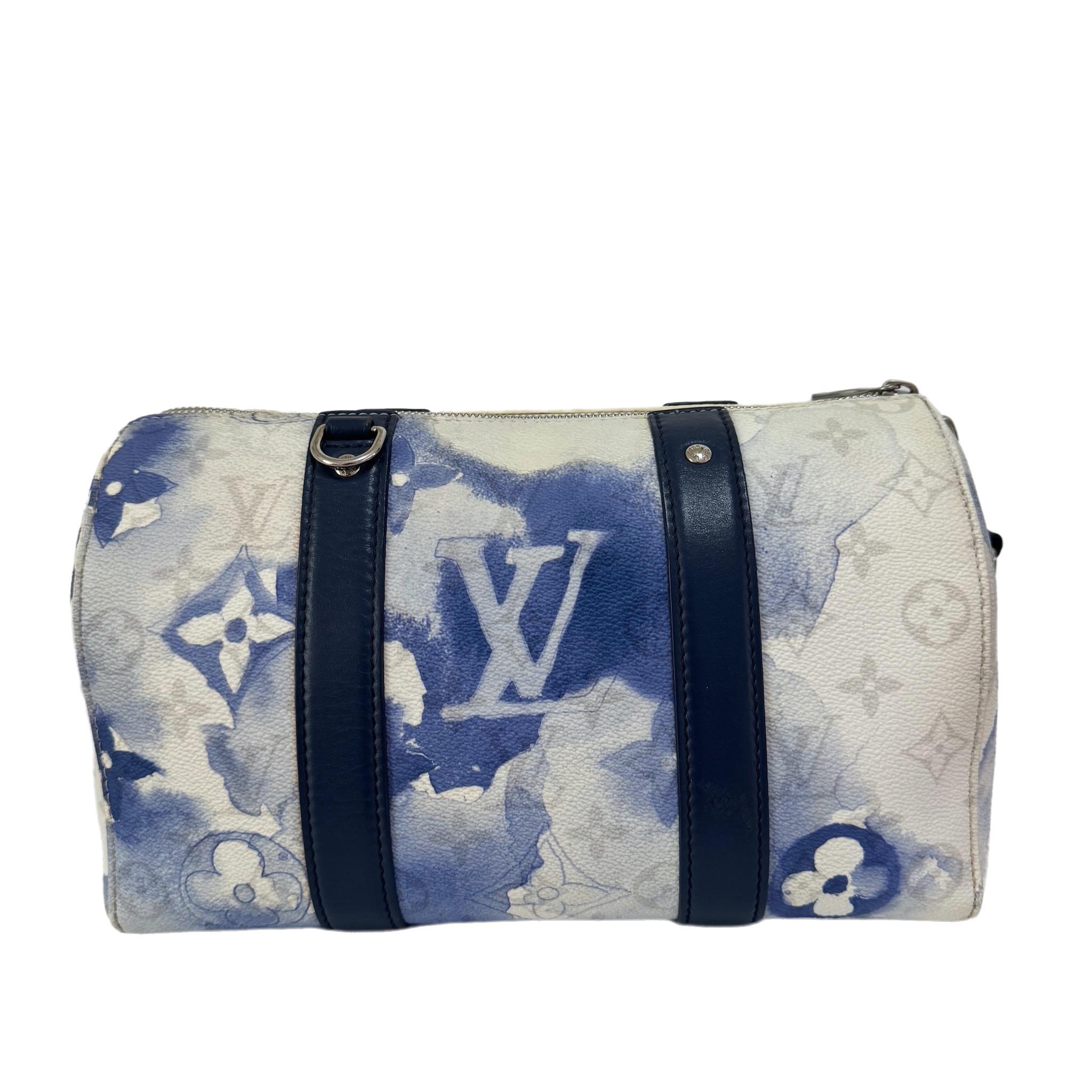 Keepall XS is a mini version of the popular Louis Vuitton Keepall. Crafted from PU and leather, this authentic Louis Vuitton handbag has blue watercolor print, adorned with navy leather, silver hardware, blue tag. Equipped with an adjustable