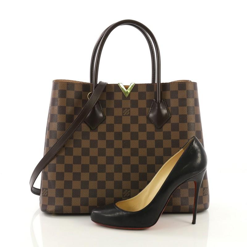 This Louis Vuitton Kensington Handbag Damier, crafted from damier ebene coated canvas, features dual rolled tall leather handles, cut-out gold-tone V on its top center, side snap closures, and gold-tone hardware. It opens to a light pink microfiber