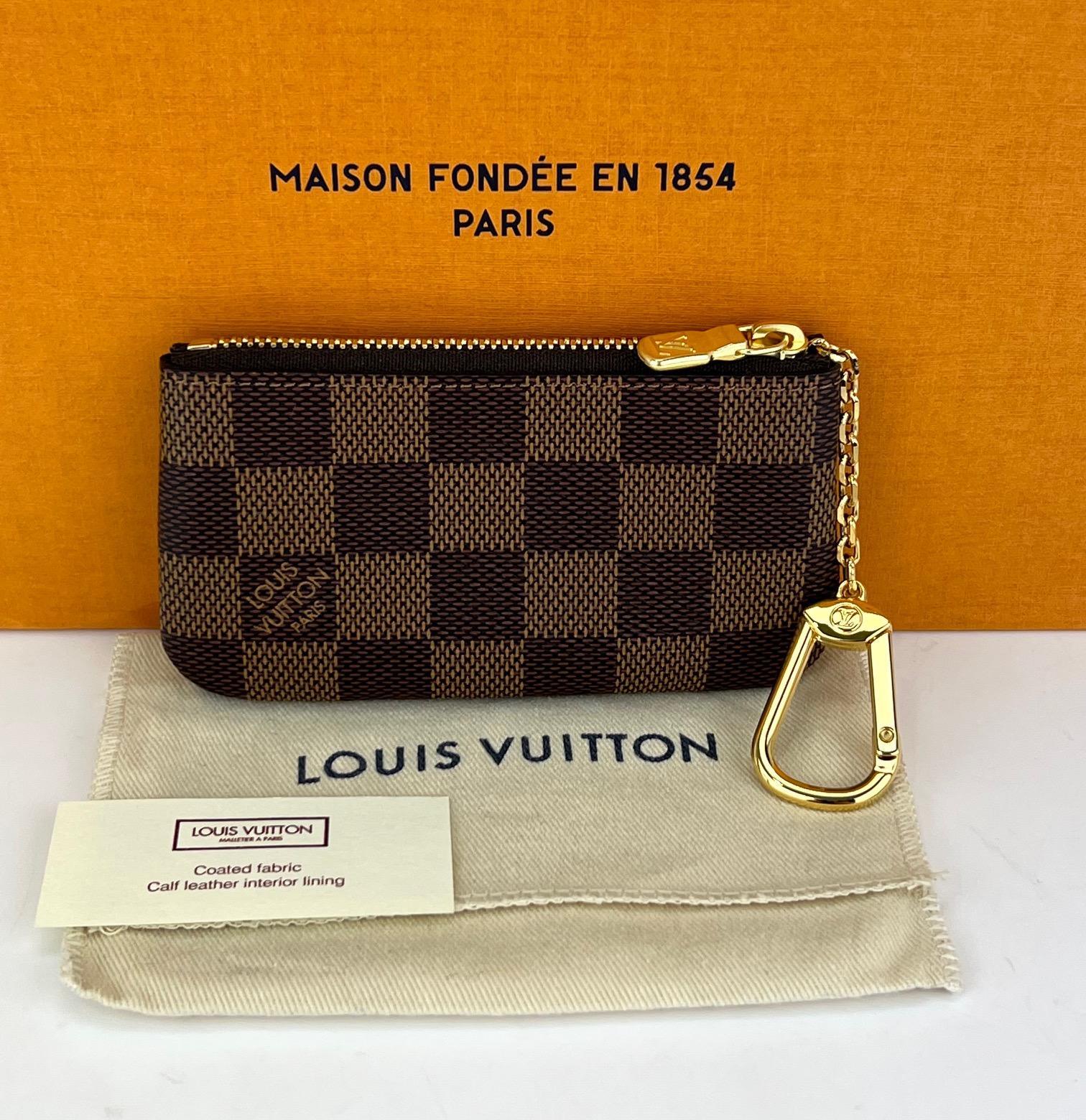 Preowned 100% AUTHENTIC
Louis Vuitton Key Pouch Damier Ebene
Use as a Bag Charm, Tiny Clutch, or Key Chain 
RATING: A...excellent, near mint, only 
slight signs of wear
INTERIOR: tiny wear by letters
DATE CODE: SD3231
MATERIAL: Damier ebene