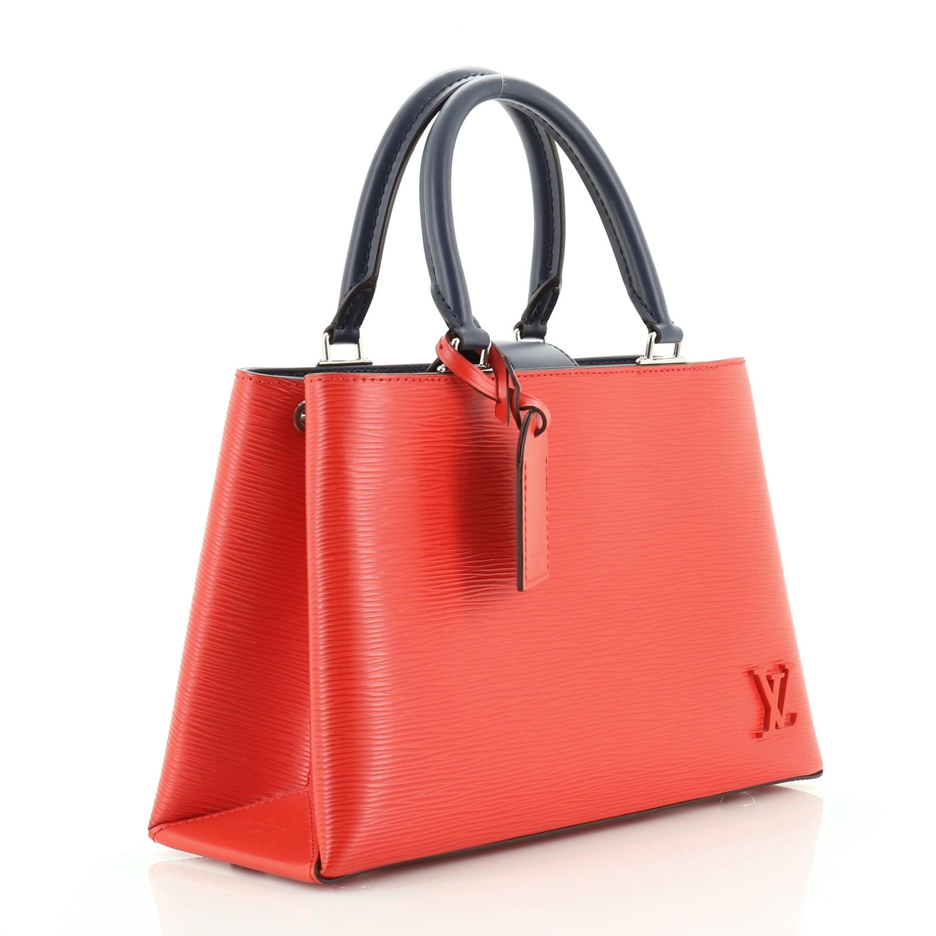 This Louis Vuitton Kleber Handbag Epi Leather PM, crafted in blue and red epi leather, features dual rolled handles, exterior back pocket, and silver-tone hardware. Its magnetic snap closure opens to a blue microfiber interior divided into two