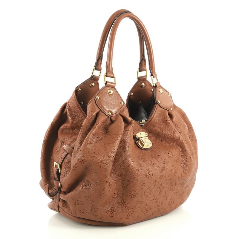 This Louis Vuitton L Hobo Mahina Leather, crafted from brown monogram perforated mahina leather, features dual rolled handles, side belt strap, protective base studs, and gold-tone hardware. Its engraved flap push-lock closure opens to a brown