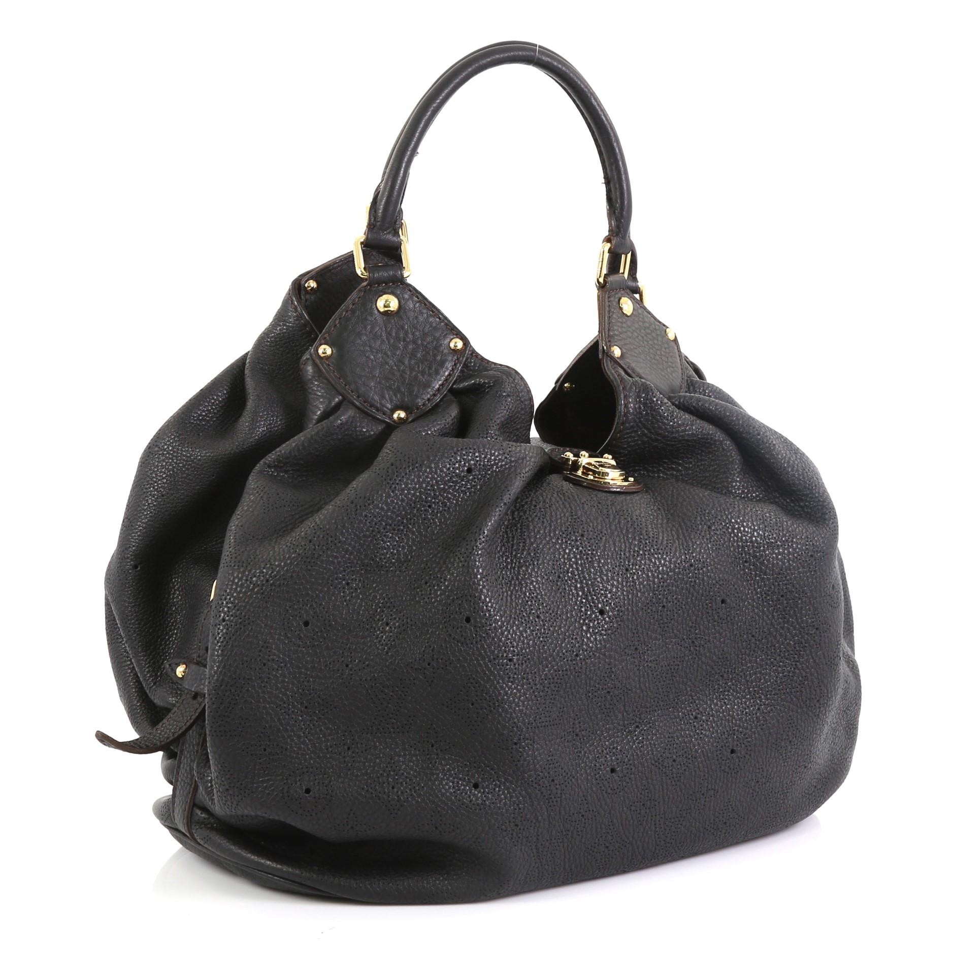 This Louis Vuitton L Hobo Mahina Leather, crafted from black monogram perforated mahina leather, features dual rolled handles, buckle and stud details, side belt straps, protective base studs, and gold-tone hardware. Its engraved top flap push-lock