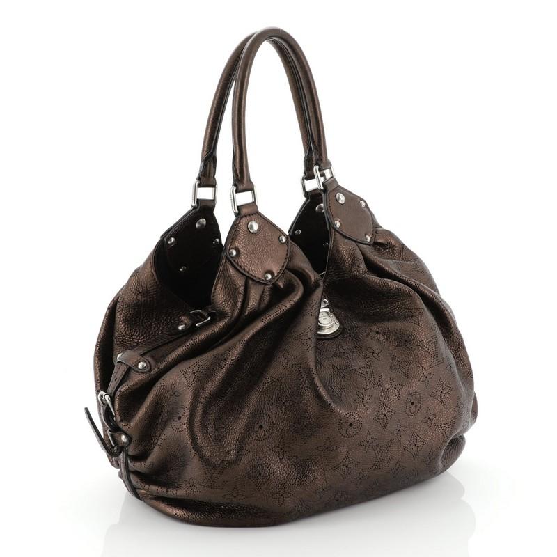This Louis Vuitton L Hobo Mahina Leather, crafted from metallic brown monogram perforated mahina leather, features dual rolled handles, buckle and stud details, side belt straps, protective base studs, and silver-tone hardware. Its engraved top flap