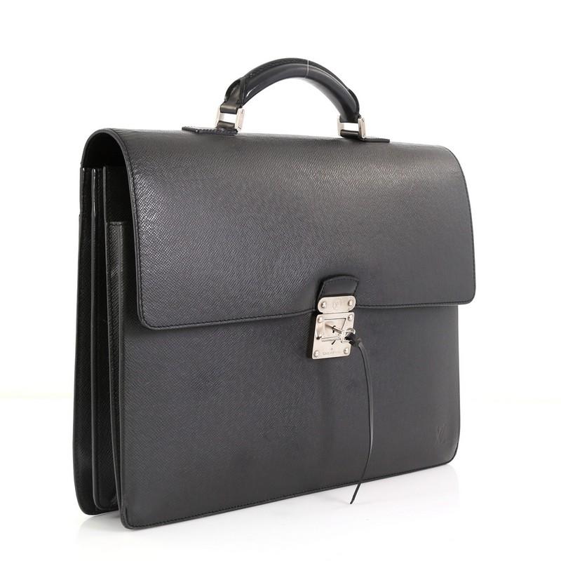 This Louis Vuitton Laguito Handbag Taiga Leather, crafted from black taiga leather, features a leather handle, S-lock flap closure, subtle LV stamped logo, exterior back flat pocket and aged silver-tone hardware. Its S-lock closure opens to a black