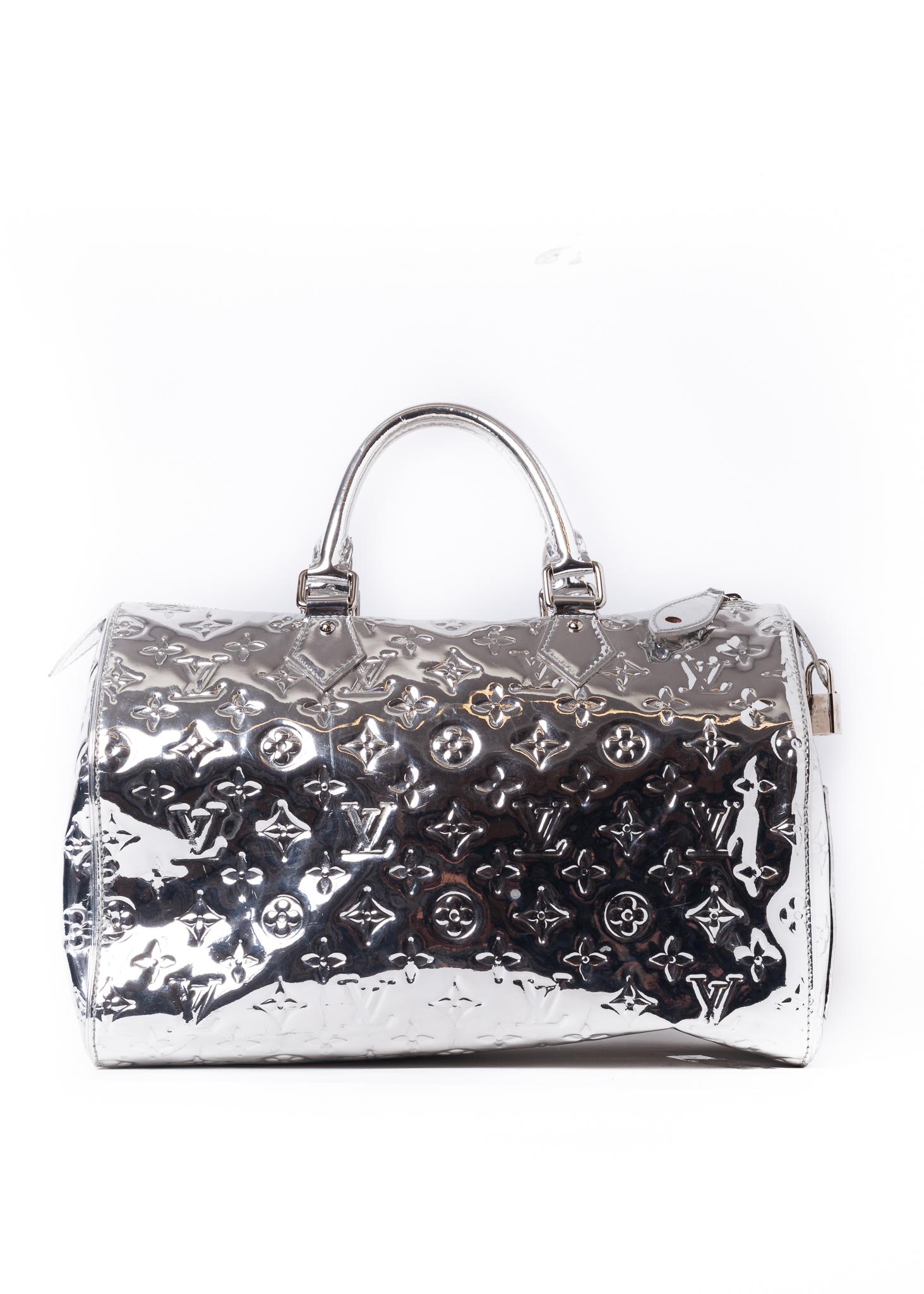 This limited edition Louis Vuitton Speedy 35 bag is made with a shiny silver monogram mirrored vinyl exterior with patent leather trim. This celebrity-coveted bag has woven fabric interior lining with two slip pockets.