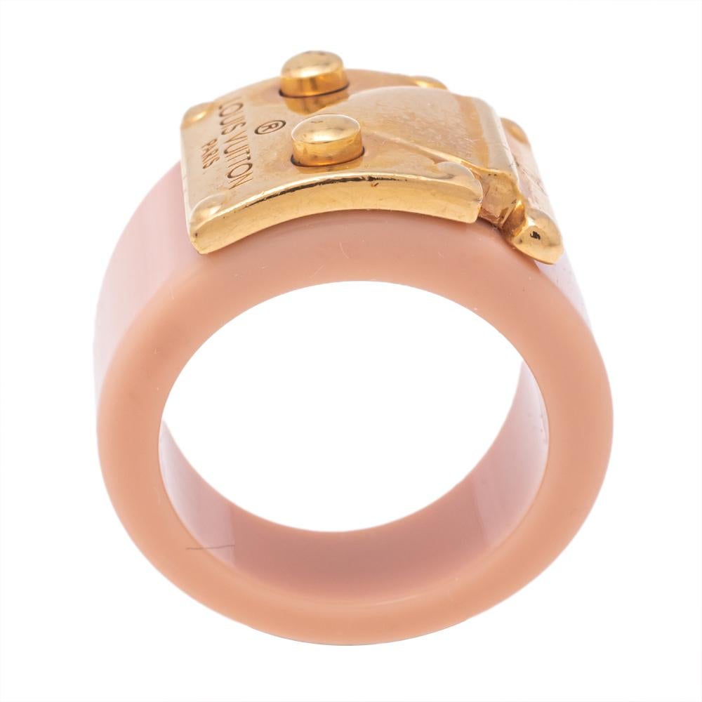 Constructed in a blush pink resin band, this Louis Vuitton Lock Me ring has a statement appeal. It has a wide size and the signature lock in gold-tone acts as the highlight of the design.