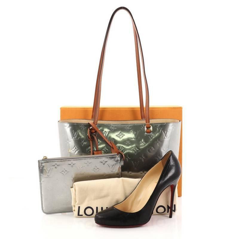 This authentic Louis Vuitton Long Beach Tote Monogram Vernis PM from 2017 goes everywhere in style, from city to beach. crafted in silver monogram vernis leather, this modern tote features dual-slim leather handles, protective base studs and