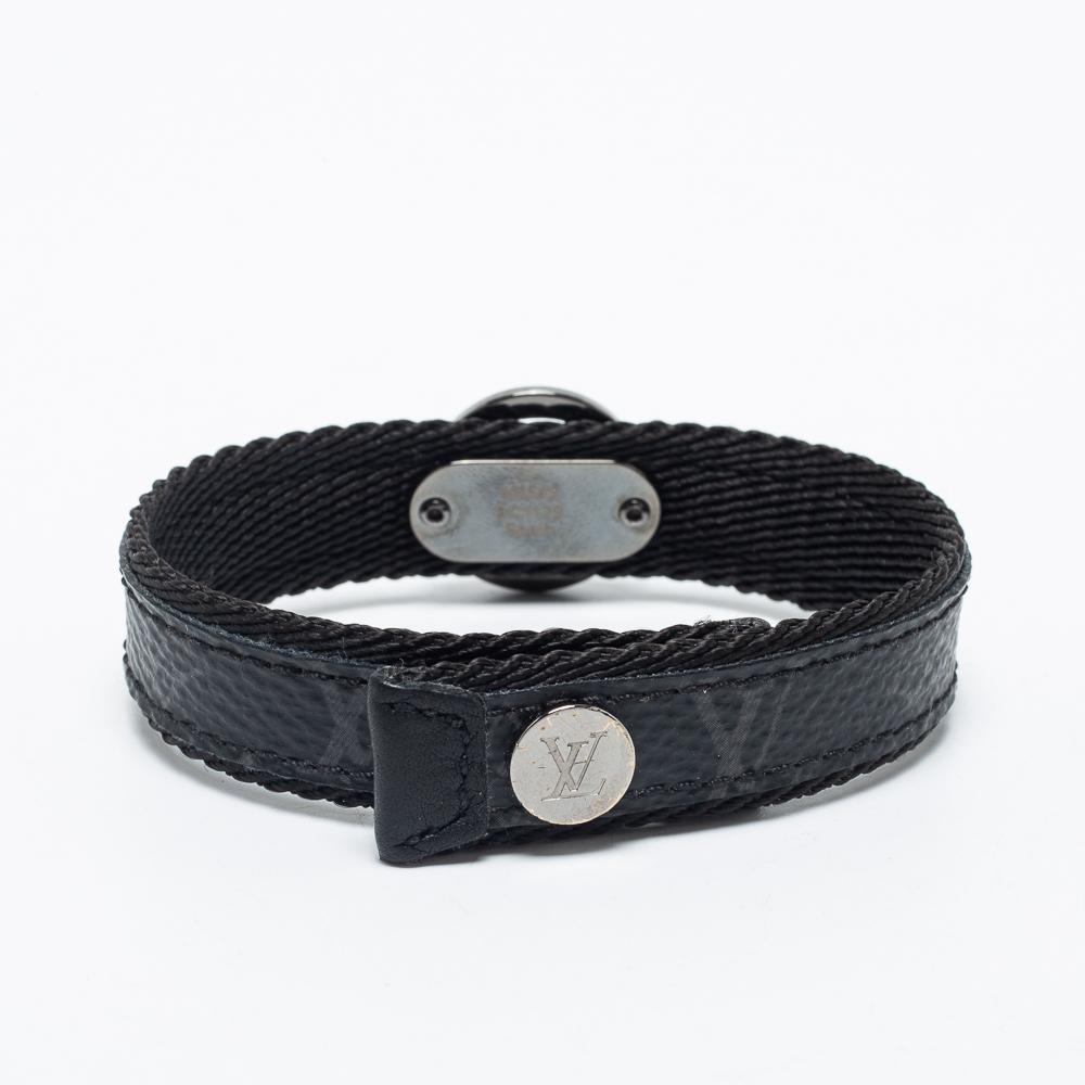 Louis Vuitton's bracelet brings a vintage yet stylish appeal to your look. Gleaming with iconic brand symbols, this bracelet is fashioned in Monogram Eclipse canvas, with a circular LV motif perched on the front. Fitted with metal accents, this