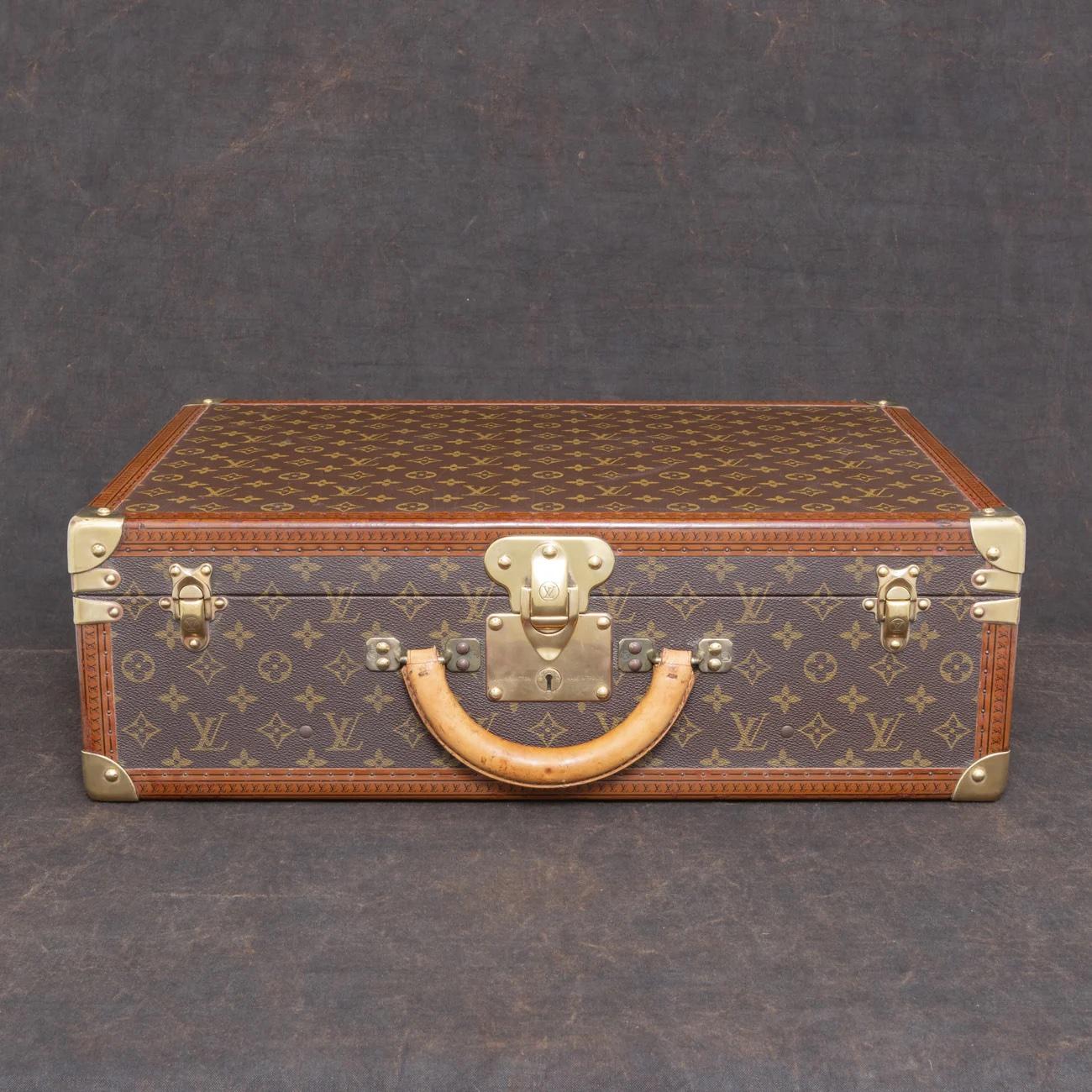 Louis Vuitton large ‘Bisten’ suitcase in LV monogram pattern coated canvas with edges trimmed in lozine and polished brass fittings.

Securing the lid of the case is a central sprung catch with a lock, accompanied by two additional latches. The